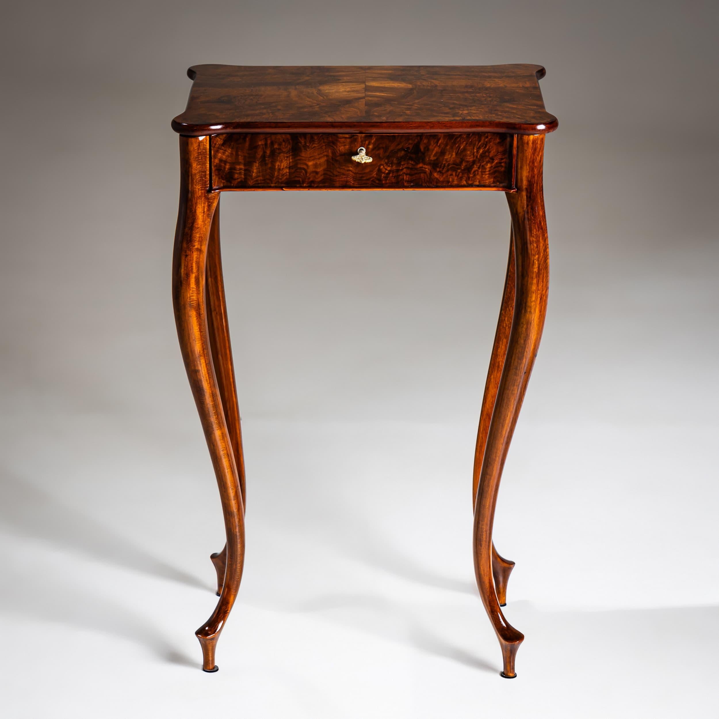 Delicate sewing table standing on slender, elegantly curved legs, crafted from finely polished walnut with beautiful veneer grain. The shaped top opens to reveal a meticulously organized interior with various compartments.