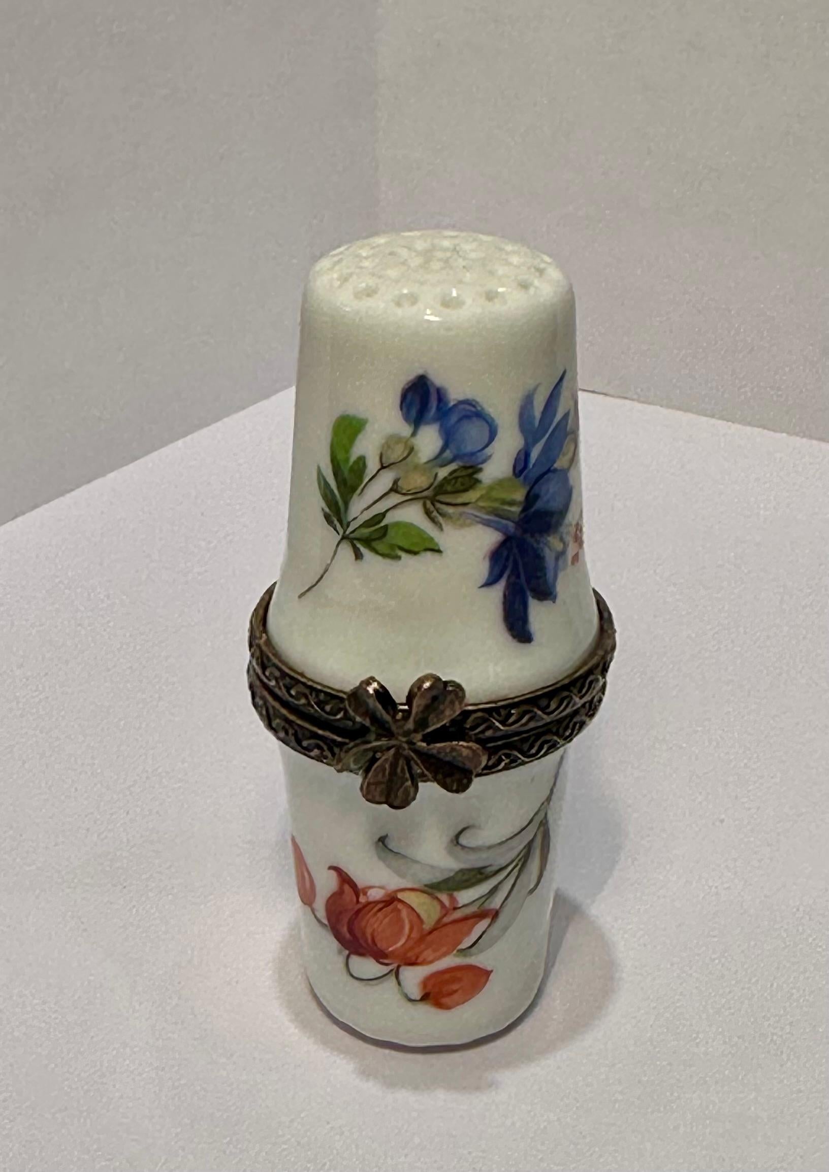 Very pretty, Limoges porcelain double thimble shaped trinket box is handmade with a white background and features pretty multi-colored flowers surrounding each side of the double thimble shaped box. This sewing themed box could also be used to hold
