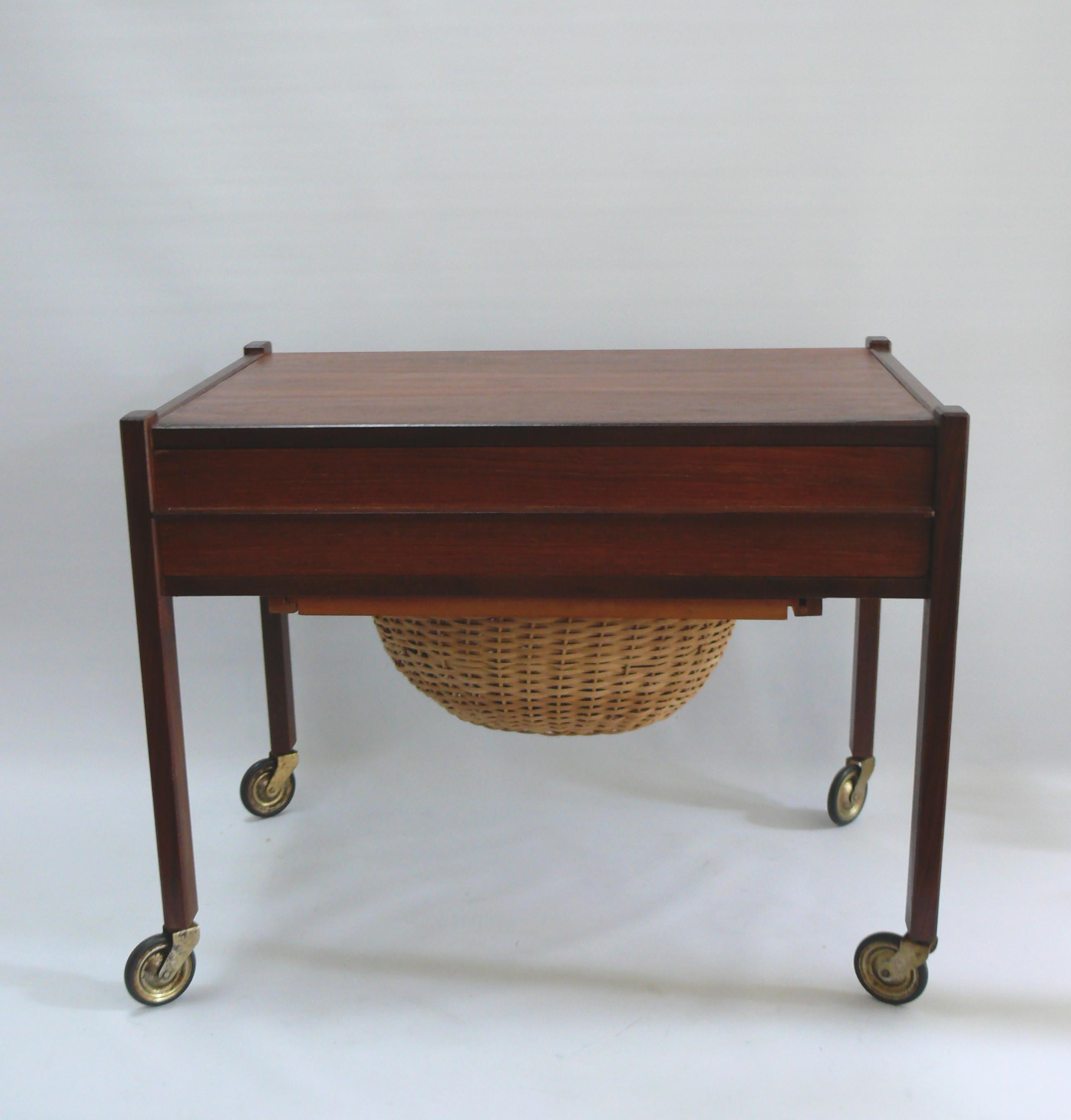 Sewing table/sewing cart, Denmark from the 1960s, teak/rosewood. Frame with solid wood legs, chipboard veneered surfaces. Drawer and a pull-out wicker basket.
Beautiful piece of furniture from Denmark from the 1960s with solid elements and casters,
