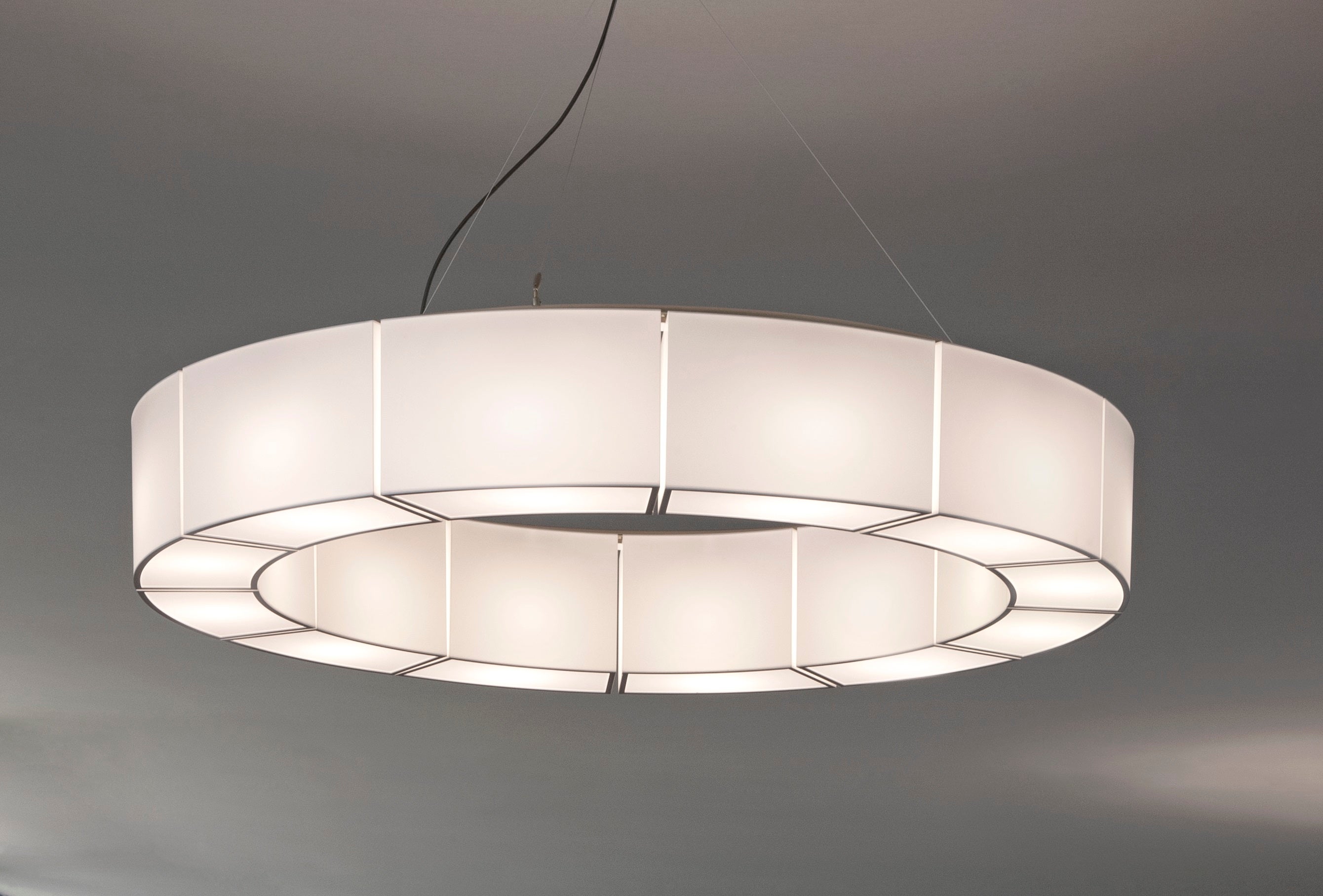 Sexta 12 pendant lamp by Miguel Milá.
Dimensions: D 128 x H 20 cm.
Materials: Metal, PVC, opal translucent methacrylate diffusers.
Available with or without opal translucent methacrylate diffusers.

This circle of double-sided shades produces a