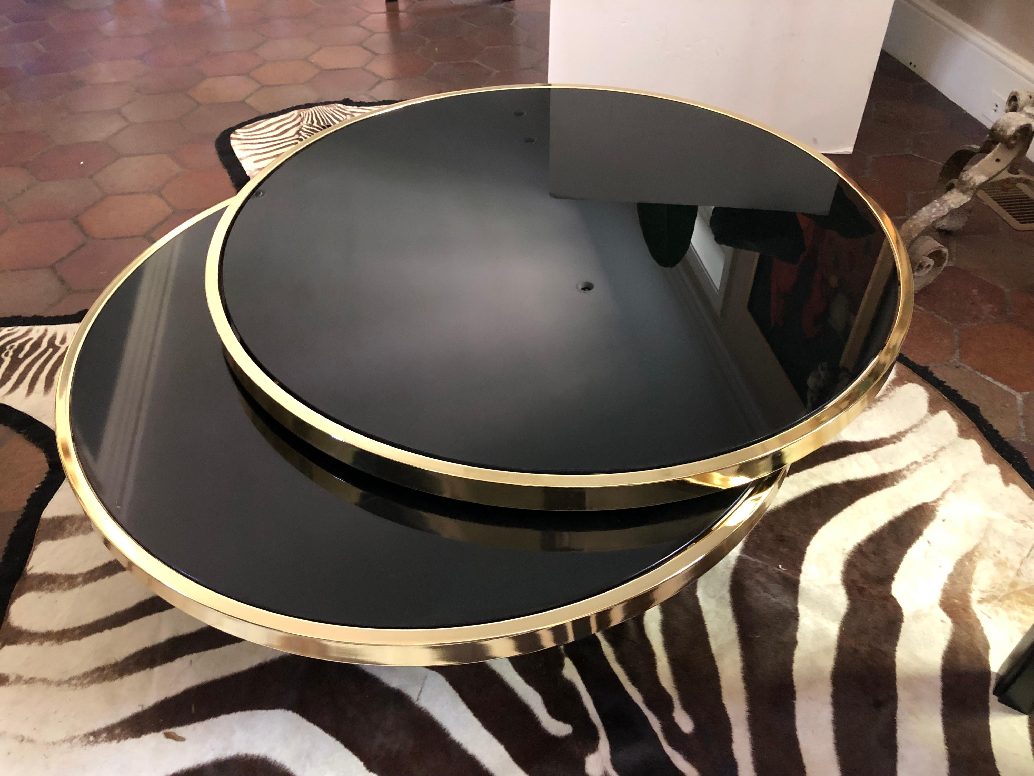 A super sexy round swivel coffee table by Design Institute of America having 2 polished brass and black glass circular surfaces on black base and flawless swivel mechanism. When fully extended the table is 5 ft wide.