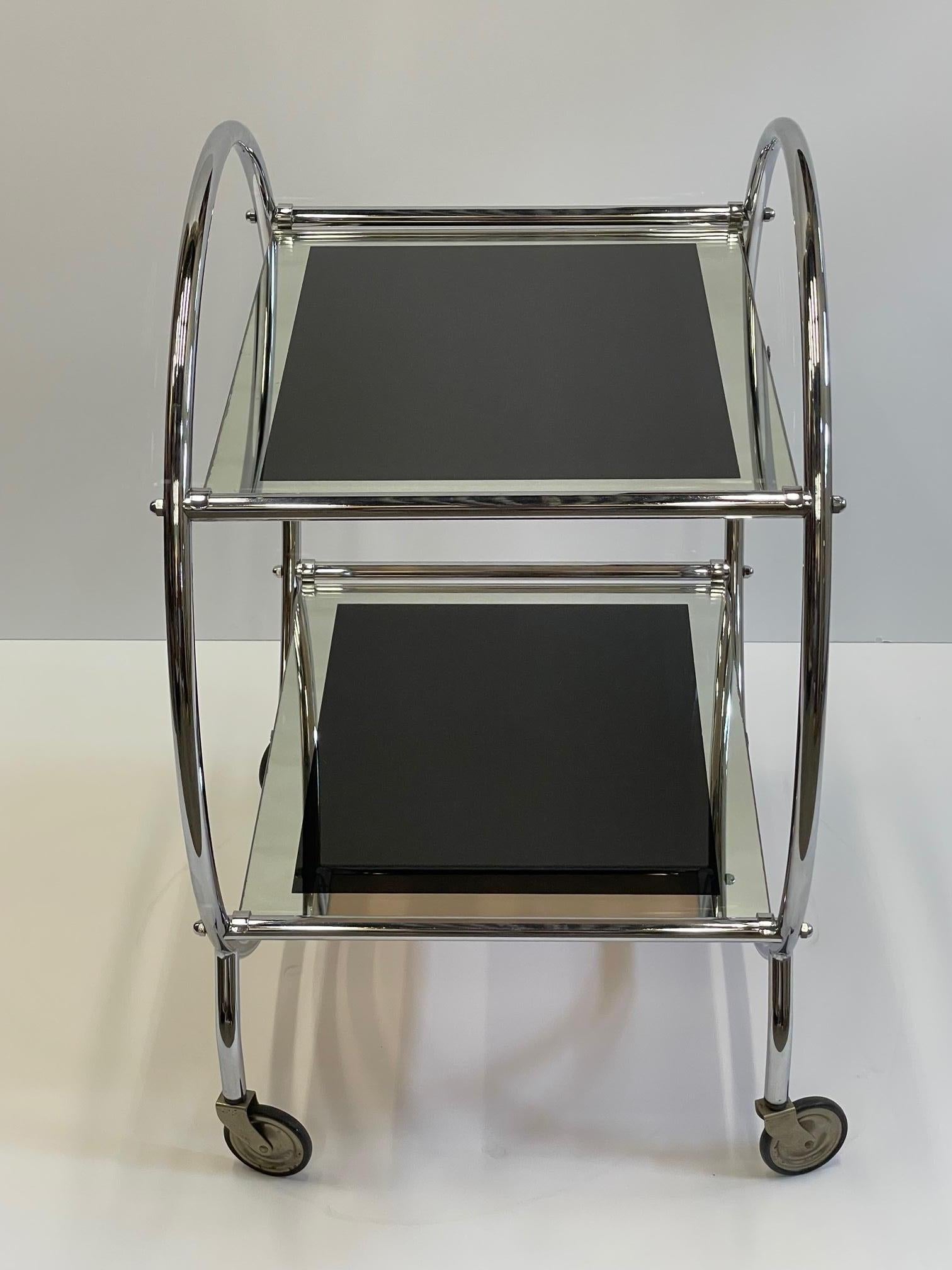 Glamorous chrome mid century modern bar cart on casters having round sides and two tiers. The glass surfaces are super sexy in black glass surrounded by mirror.
Measures: Lower shelf 10