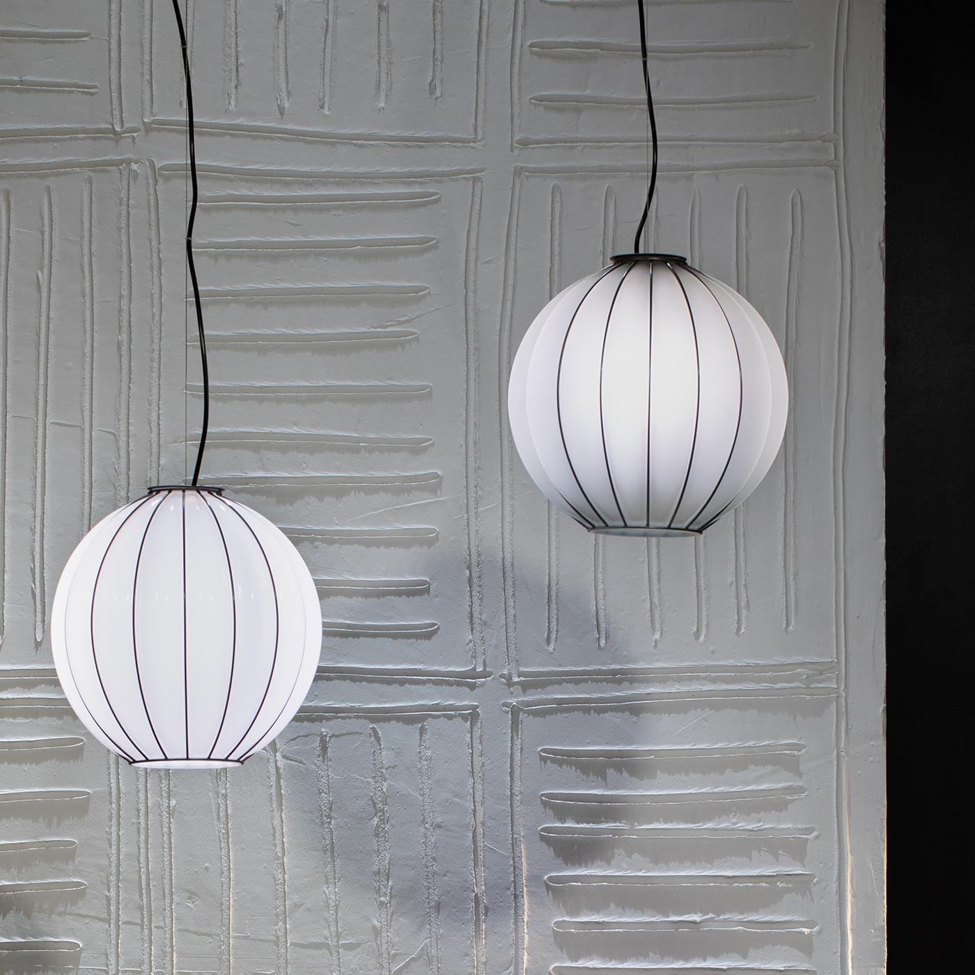 Also offered in a table counterpart allowing for cohesive displays, this precious pendant lamp reveals a clear industrial inspiration defined by the integration of a spherical diffuser in mouth-blown, white Murano glass. Master artisans blow the