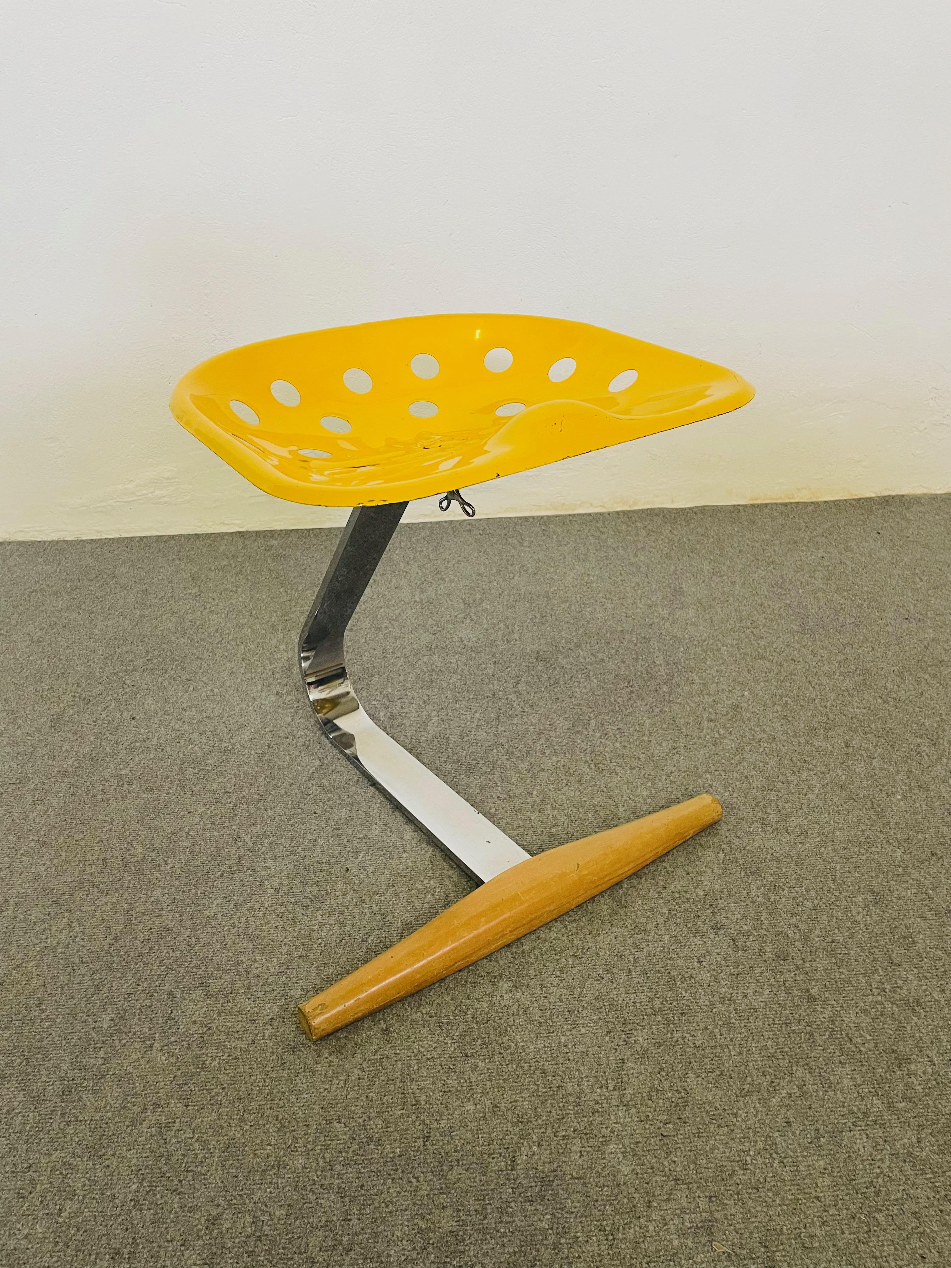 Sgabello. Stelo in acciaio cromato. Seduta laccata nel colore giallo. Poggiapiedi in faggio trattato a vapore, colore naturale.
Nel 1970 Zanotta mise in produzione la 