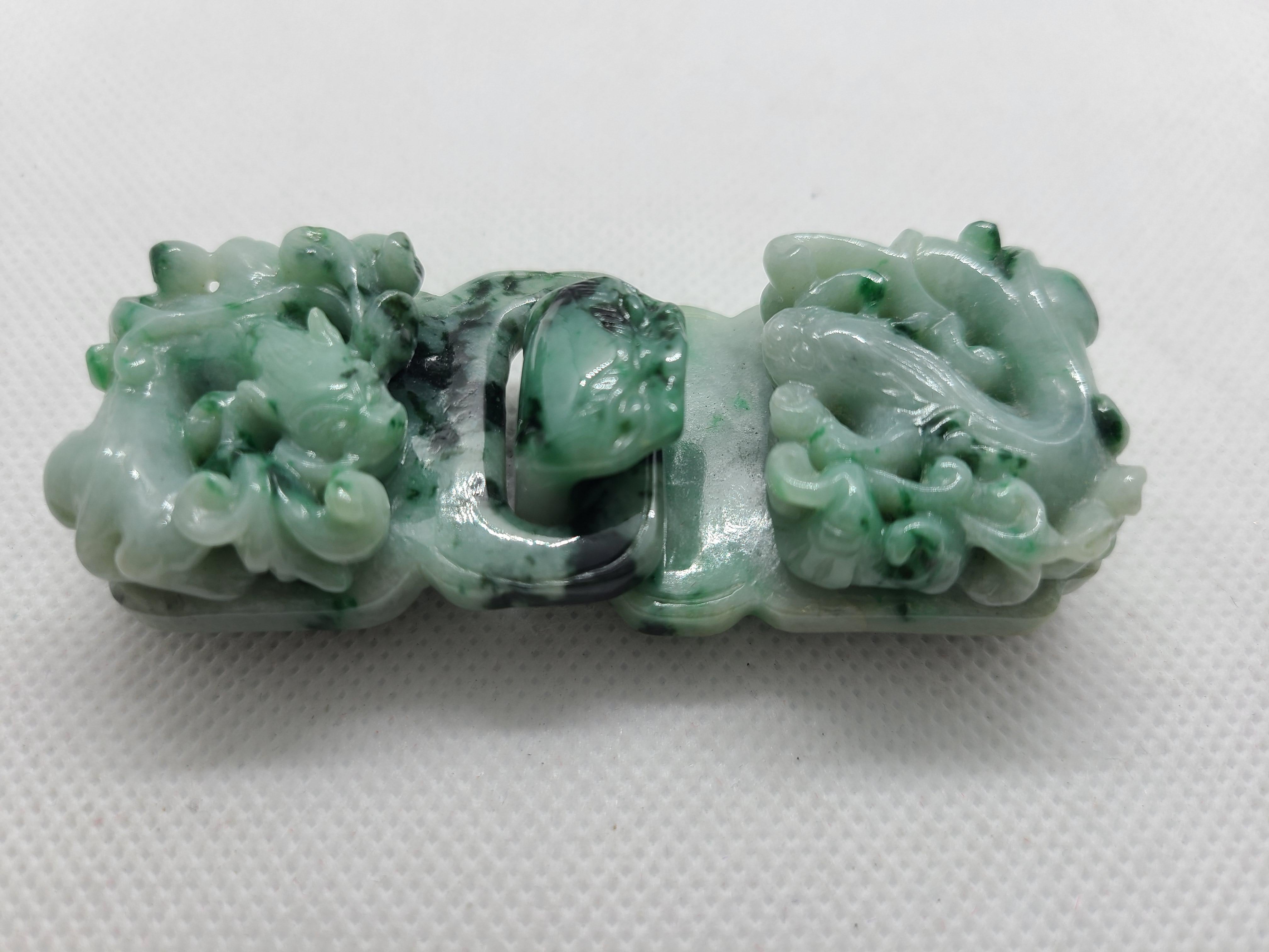 Una coppia di fibbie di giada naturale chiara, scura e verde-marrone, intricatamente scolpite con antichi draghi che si librano tra le nuvole, simbolo di pace e prosperità. Le due fibbie insieme misurano circa 8,1 x 3 x 2 cm e hanno un peso