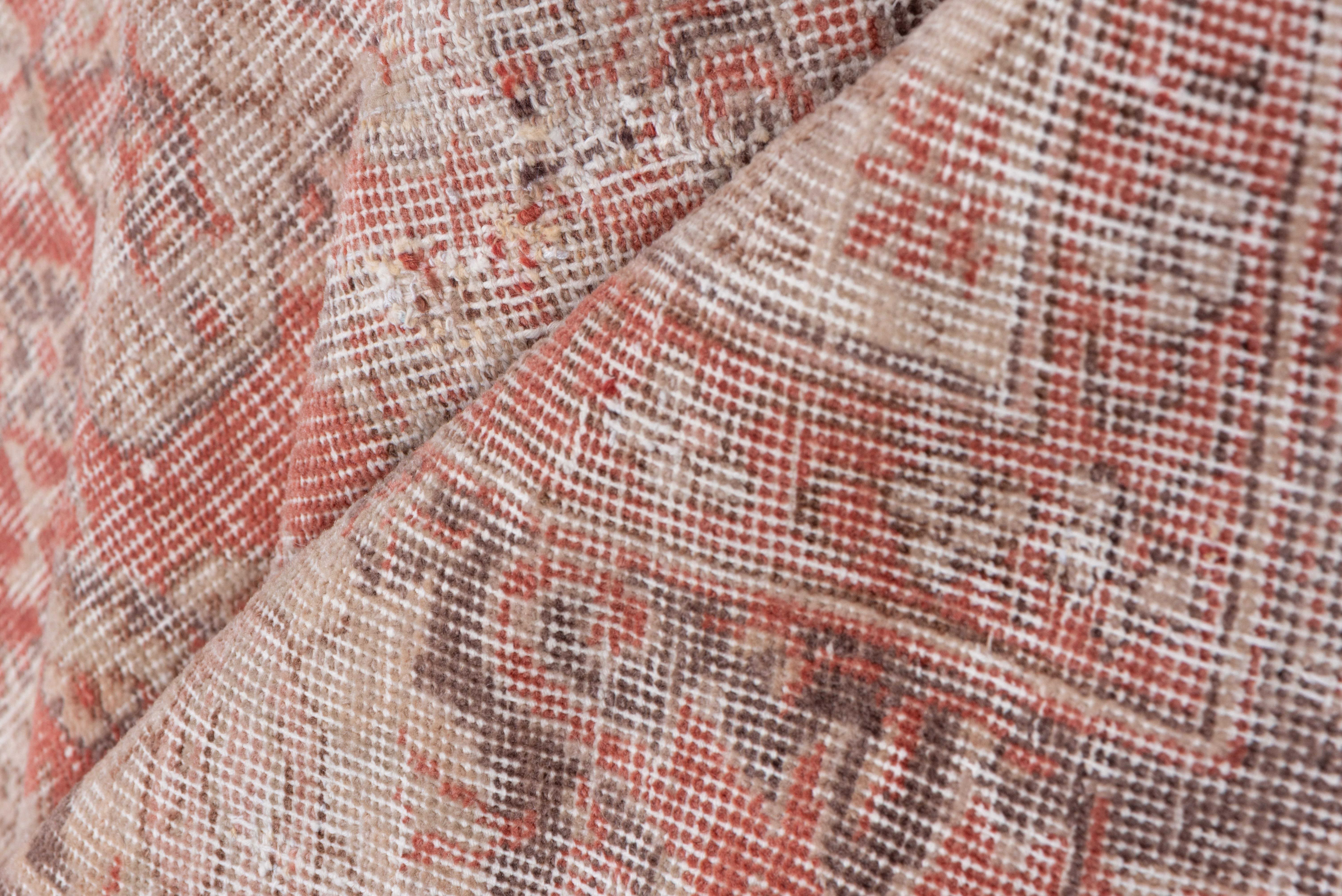 Dieser ziemlich ramponierte anatolische Stadtteppich zeigt ein hellrotes und rostfarbenes Feld mit einem Allover-Muster aus Palmetten des persischen Schah 'Abbas, mit einer dunklen Bordüre aus Palmetten und gegabelten Akanthusblättern. Einige