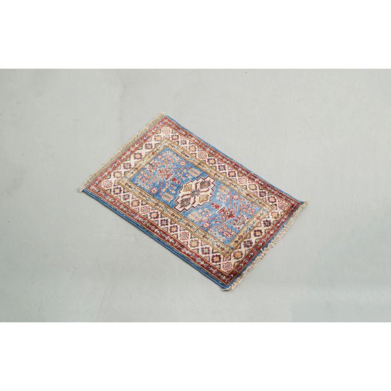 I ricchi motivi blu, bianchi e rossi e le dimensioni ridotte e compatte di questo tappeto Kazak intrecciato a mano sono ideali come tappetino in uno spazio di lavoro o all'ingresso, oppure come piccolo tappeto d'accento in un soggiorno, una camera