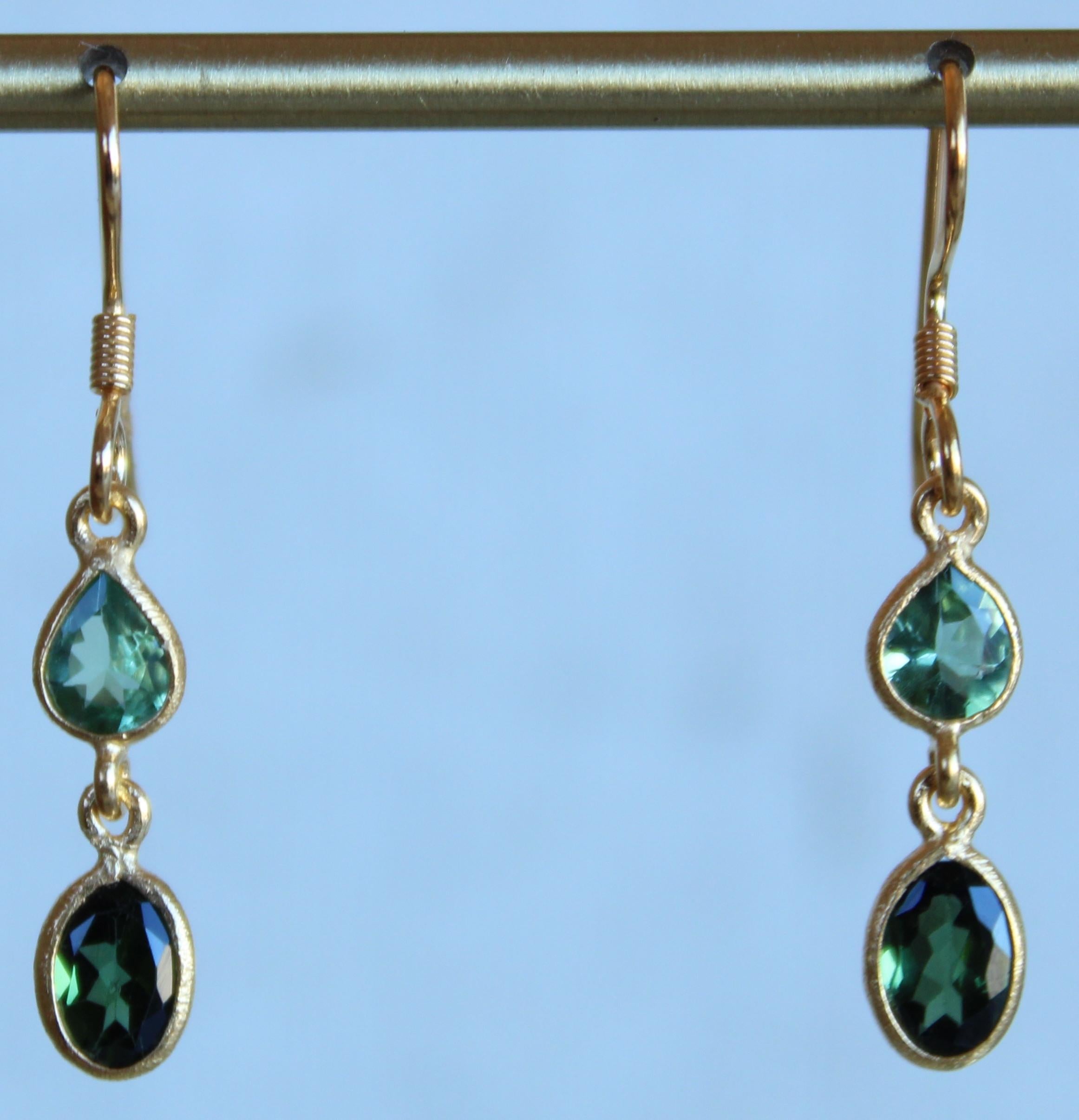 This pair of earrings are absolutely exquisite with showcasing the variations of green Tourmaline. The top stone is a seafood green Tourmaline pear while the bottom stone is a hunter green Tourmaline oval. These stones are set in a 14K gold plating