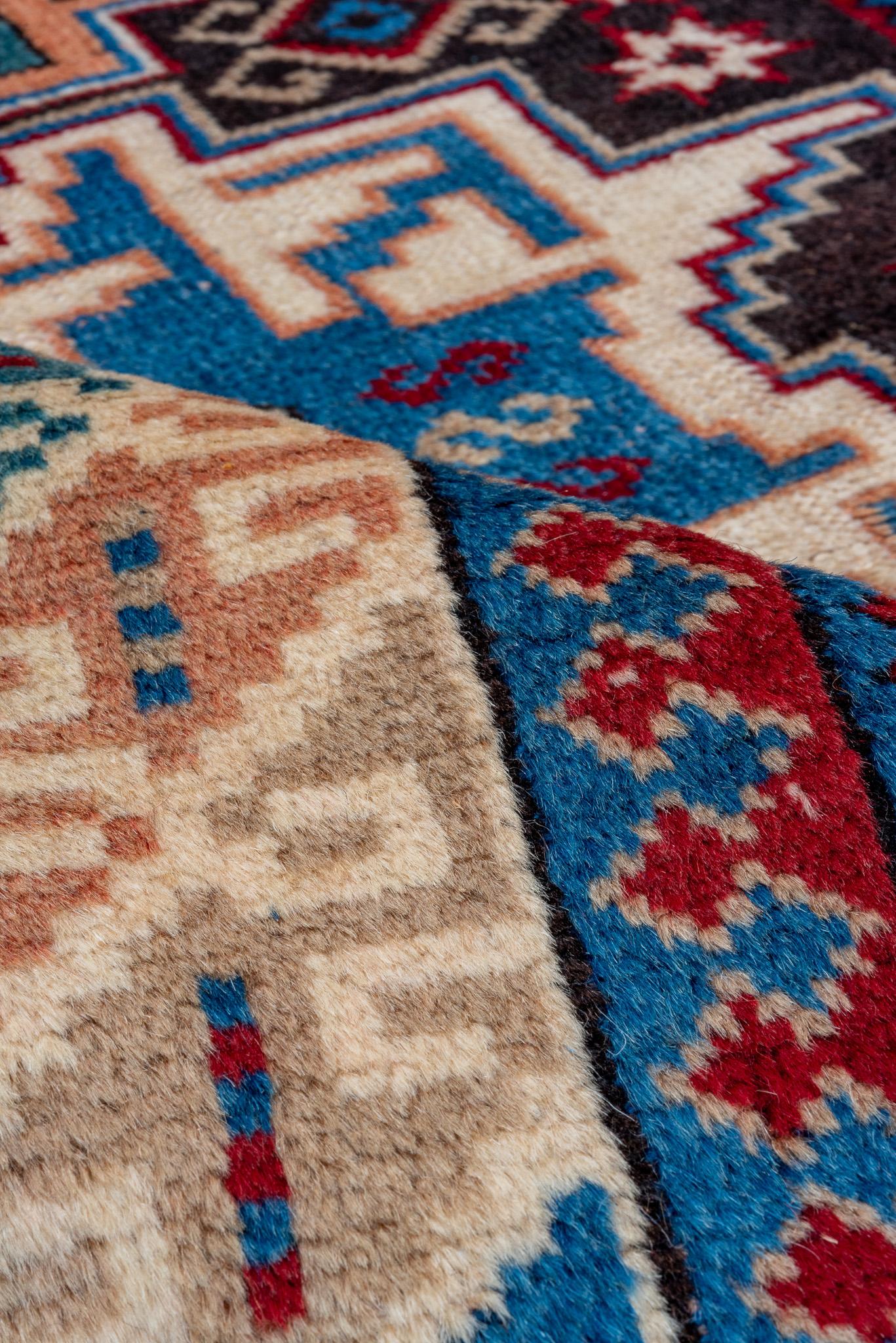 This is a striking Caucasian rug measuring 3.9 x 5.8 feet. It showcases bold geometric motifs in vibrant hues of blue, red, and ivory, set against a dark backdrop. The detailed border features traditional Caucasian patterns, adding depth and