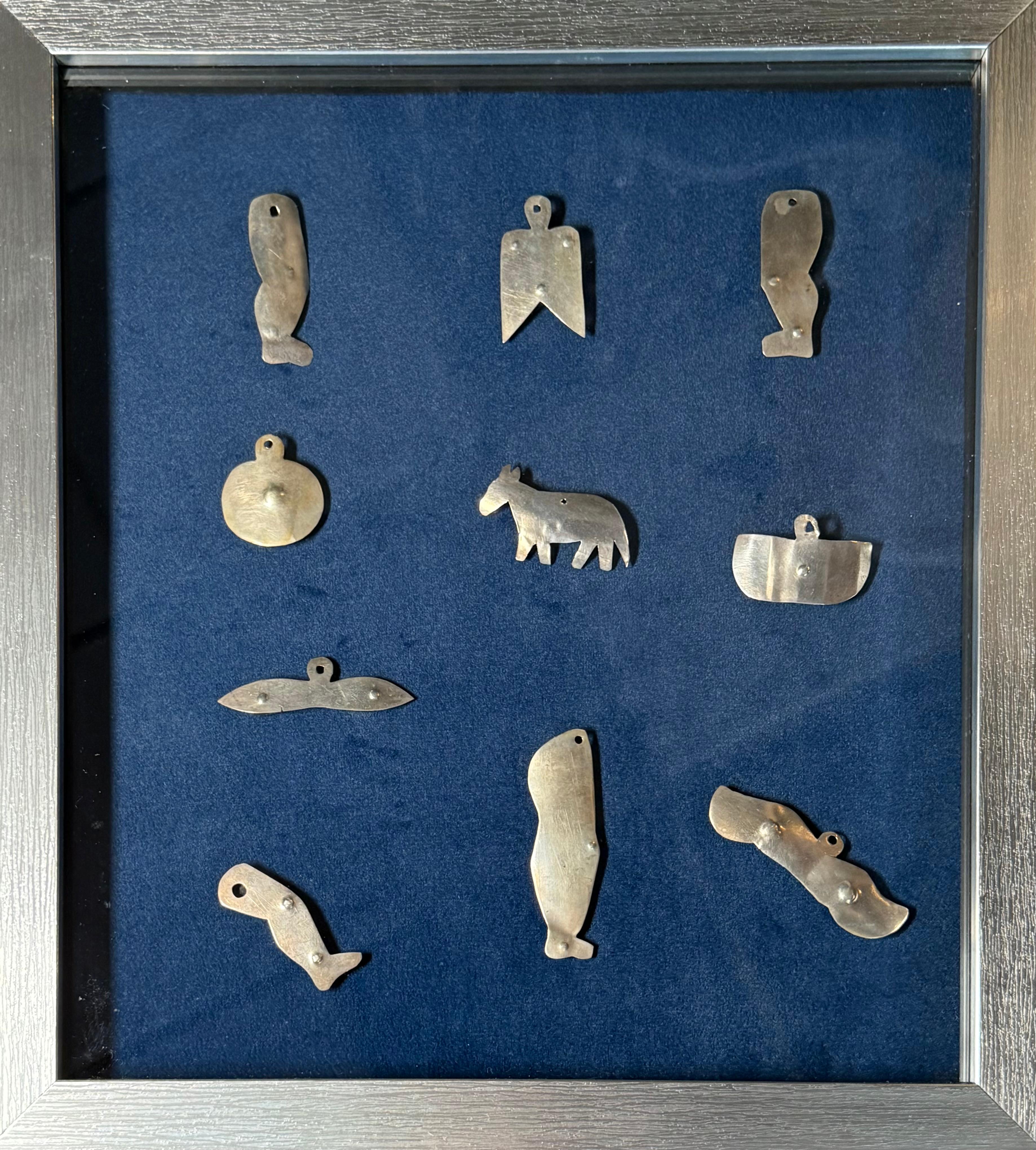 Ésta es una Colección de Charms Milagros de Puerto Rico. Representa una caja rectangular de marco plateado con fondo azul y cristal que contiene una colección de 10 dijes de milagros de metal en tono plateado. Tradicionalmente en Puerto Rico las