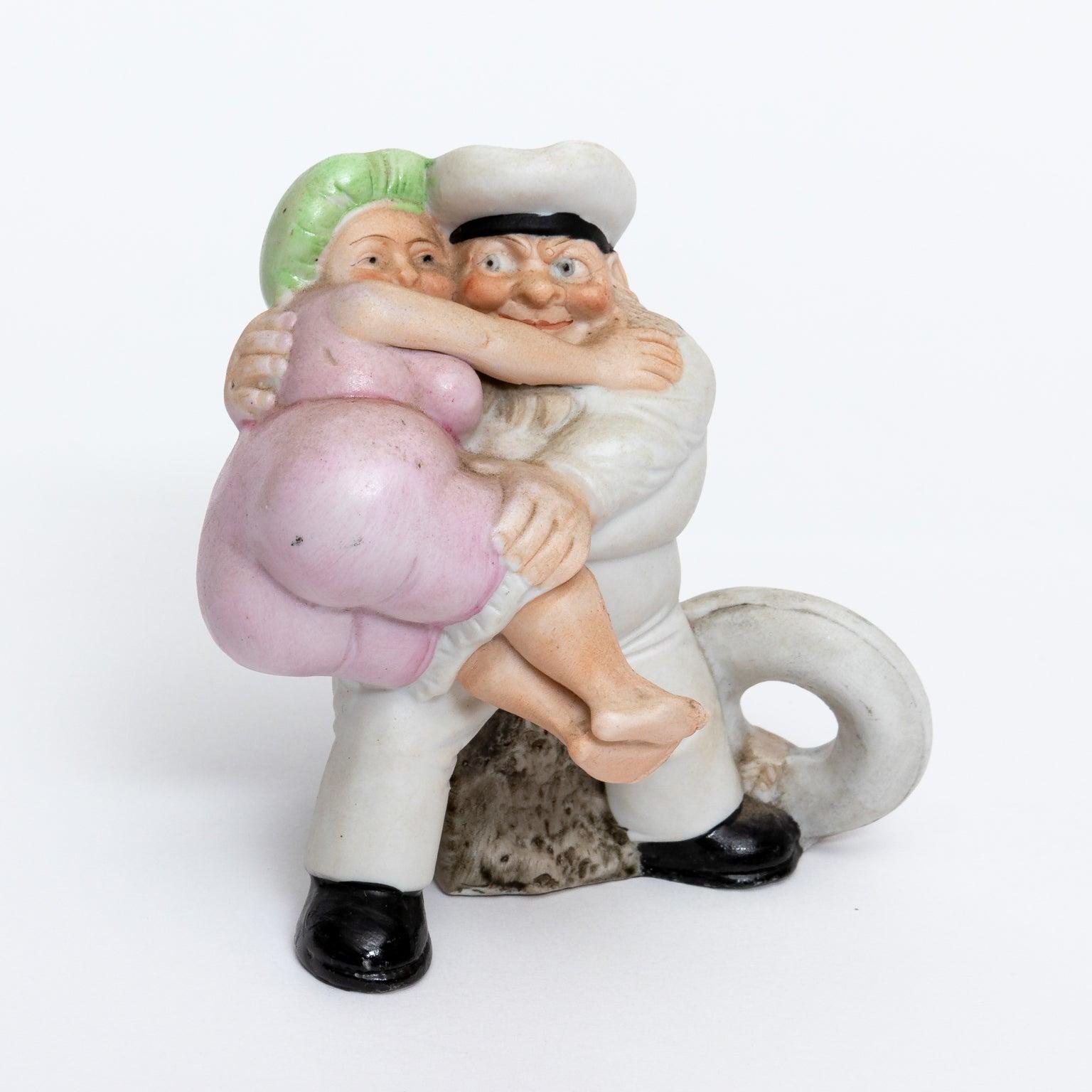 This is the  Schafer & Vater sailor joisting the ample bodied bather....The bathing beauty is wearing a yellow bathing suit and an aqua colored bathing cap. He has the life preserver behind him and it is a small container from the back. Great