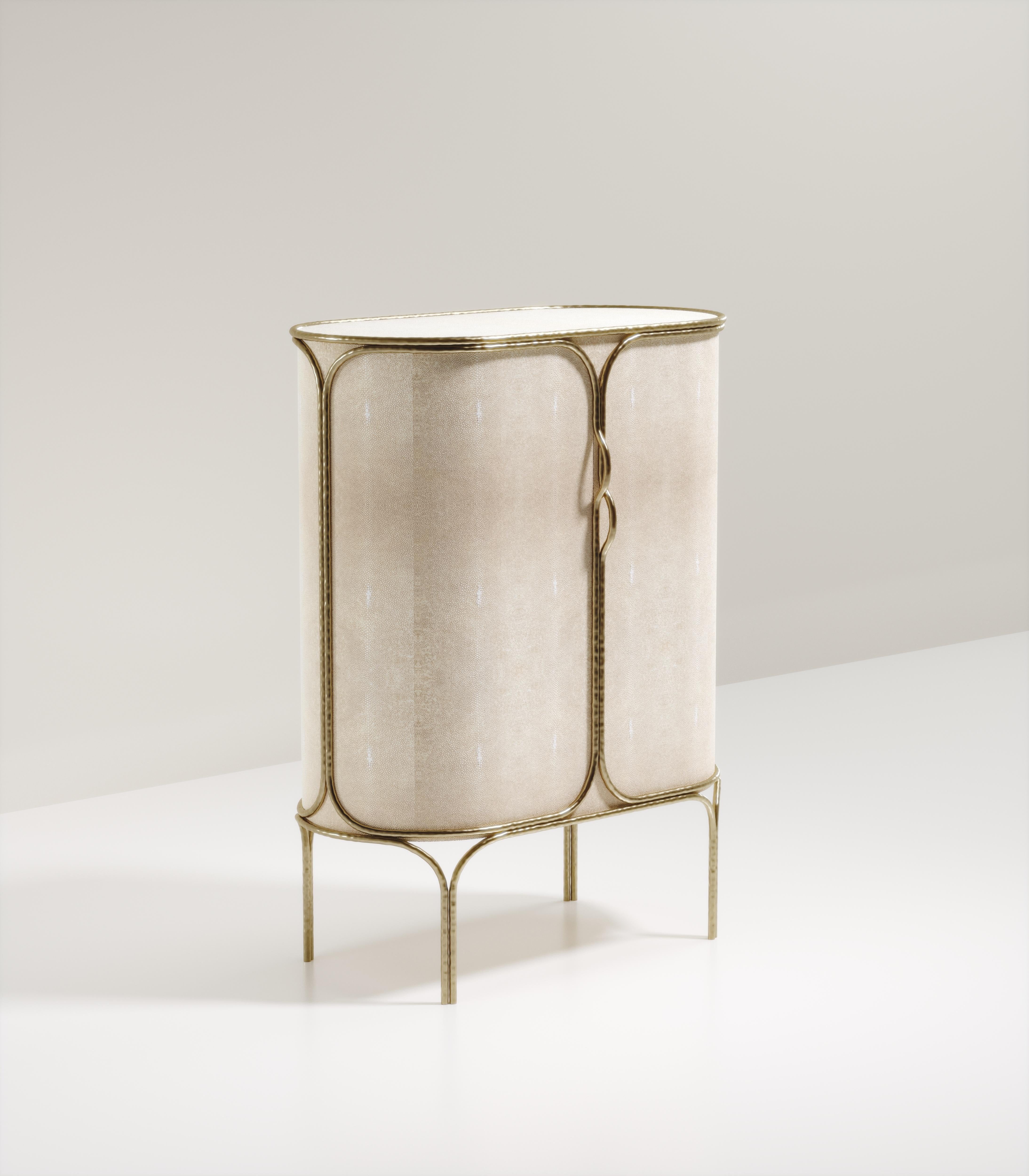 The Arianne bar cabinet by R&Y Augousti is one of a kind statement piece. The overall piece is inlaid in cream shagreen accentuated with intricate bronze-patina brass details that have the signature Augousti 