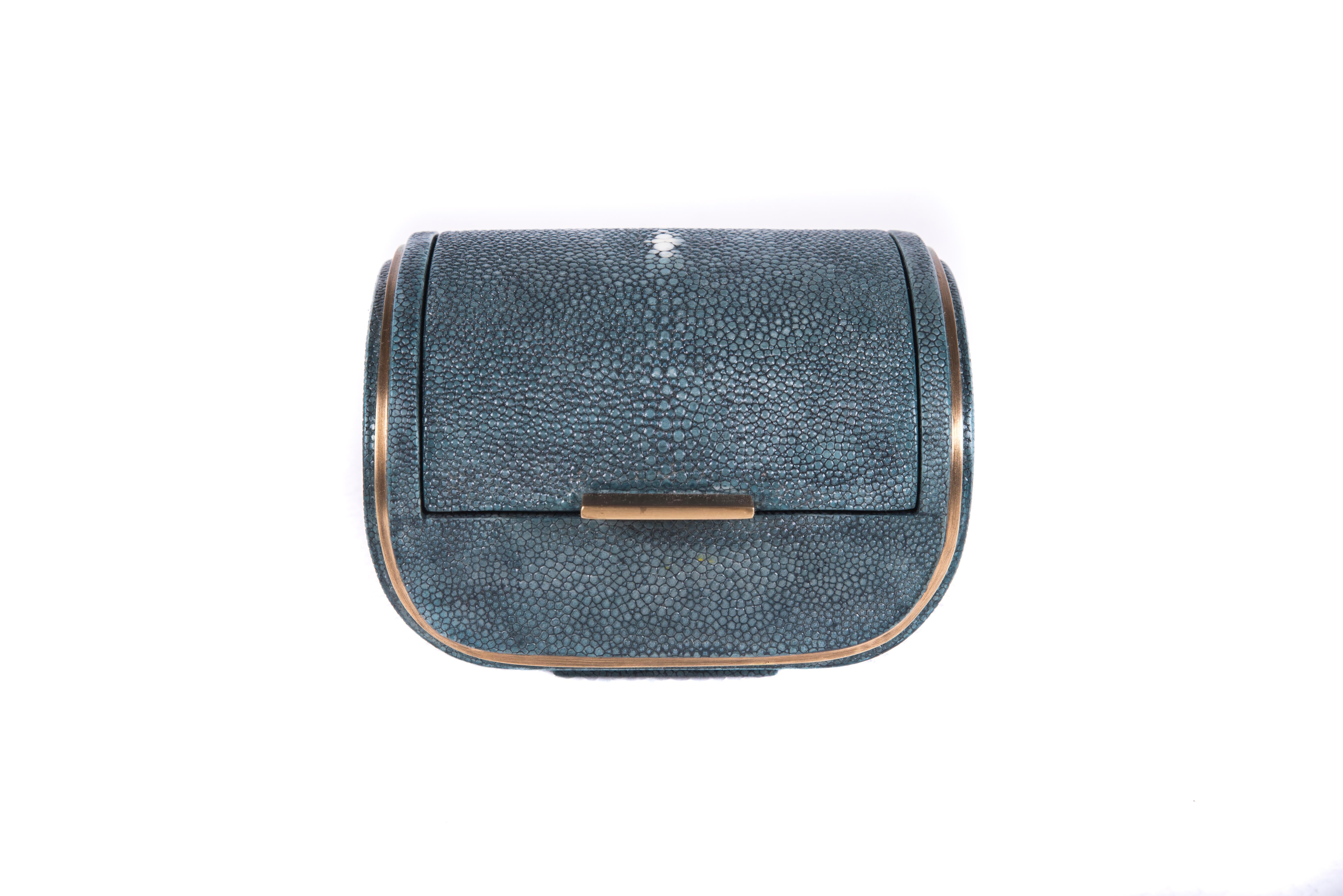 The Dandy box is a chic accent piece for your home. The piece is lined with a removable velvet tray should one wish to use it for jewelry. The piece is completely inlaid in a grey blue shagreen, with a discreet bronze-patina brass metal indentation