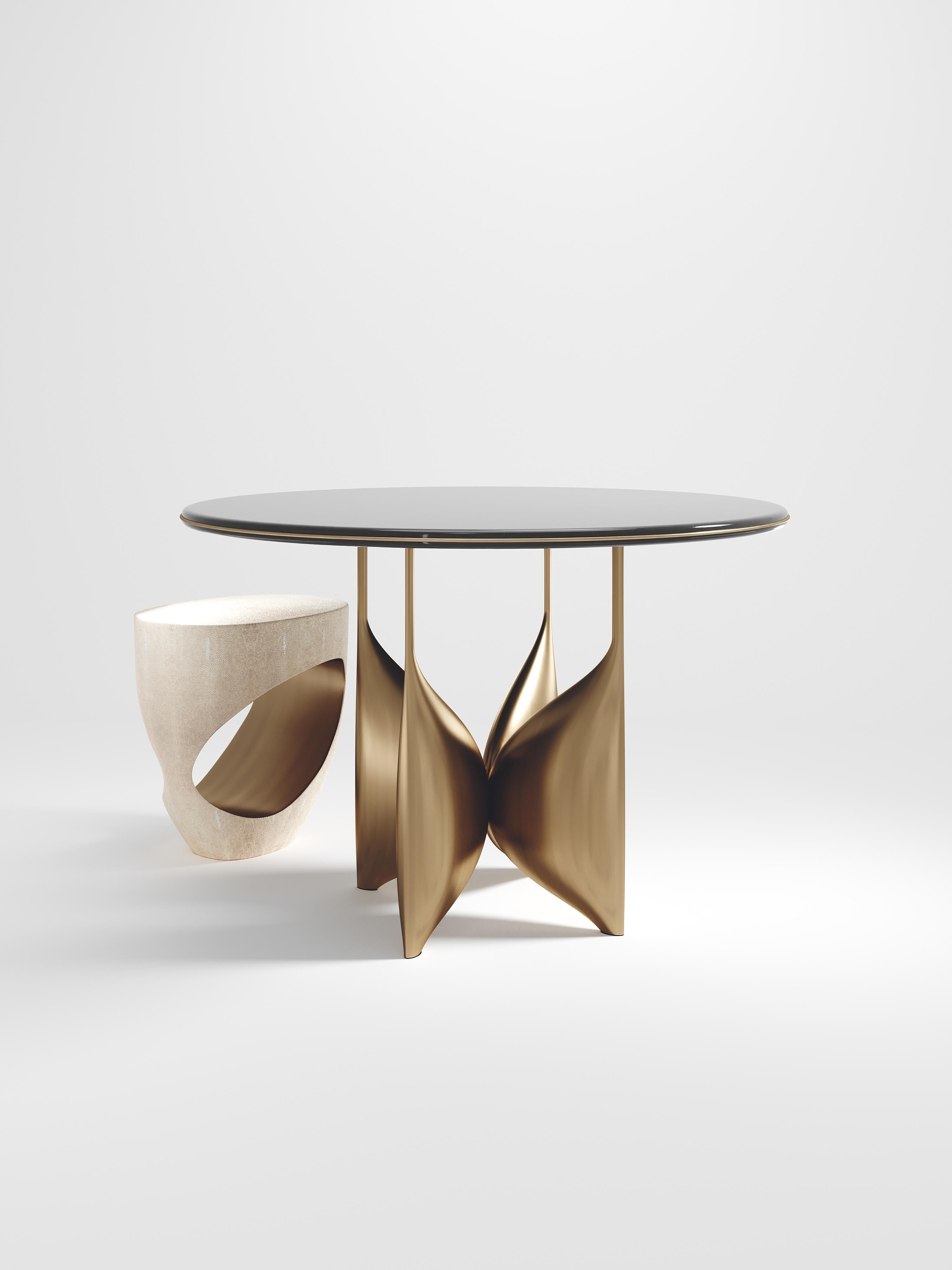 The Plumeria breakast table by Kifu Paris is a dramatic and elegant piece. The cream shagreen inlaid top sits on a sculptural bronze-patina brass base that is conceptually inspired by bird feathers floating on top of a lake. The border of the top is