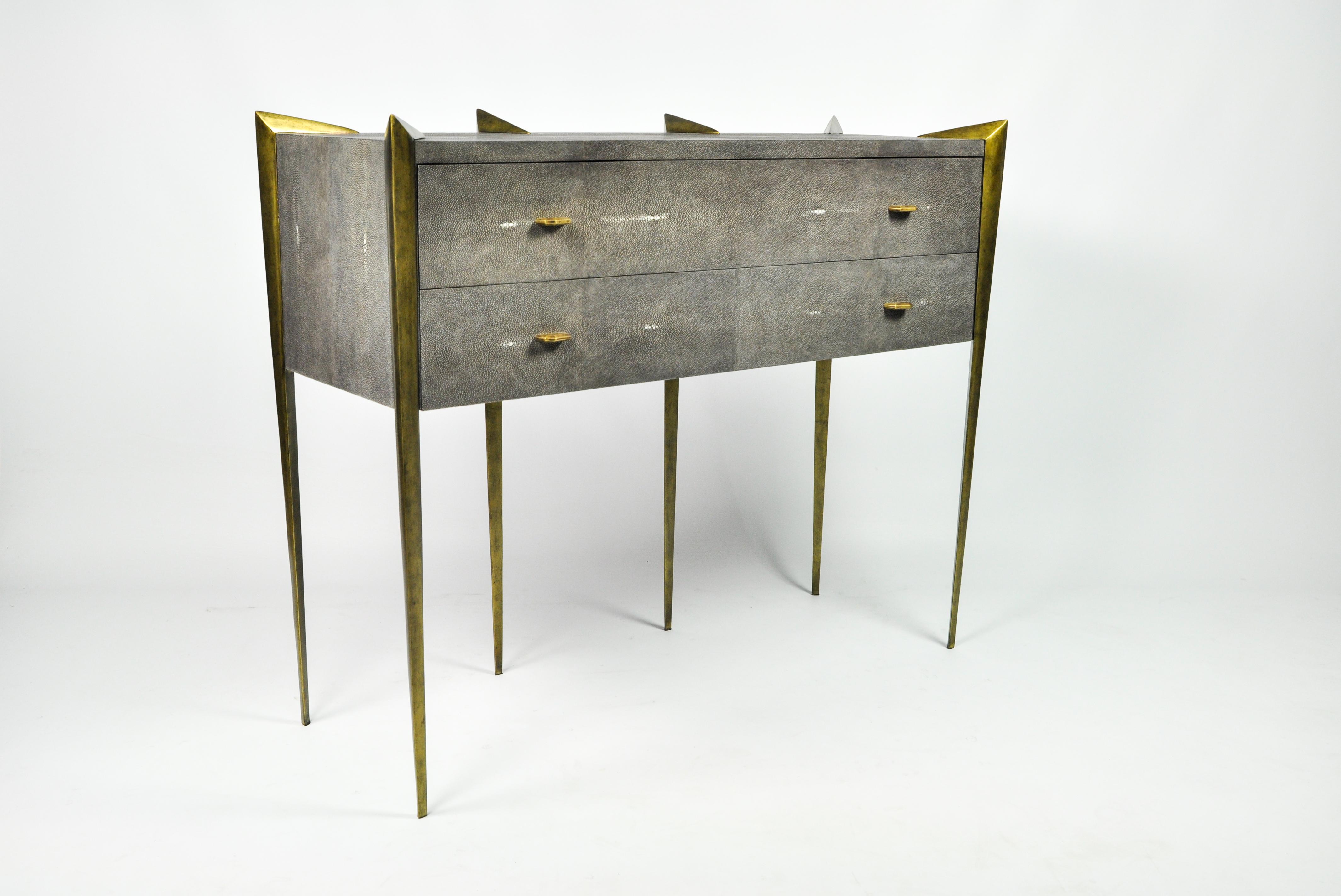 This chest of drawers from our collection CIRCINI is made of dark grey shagreen (our ref CARBON).
It has 2 drawers with brass knobs.
The case is mounted between claws and reminds a solitaire ring.
The legs have an antique brass patina.

An