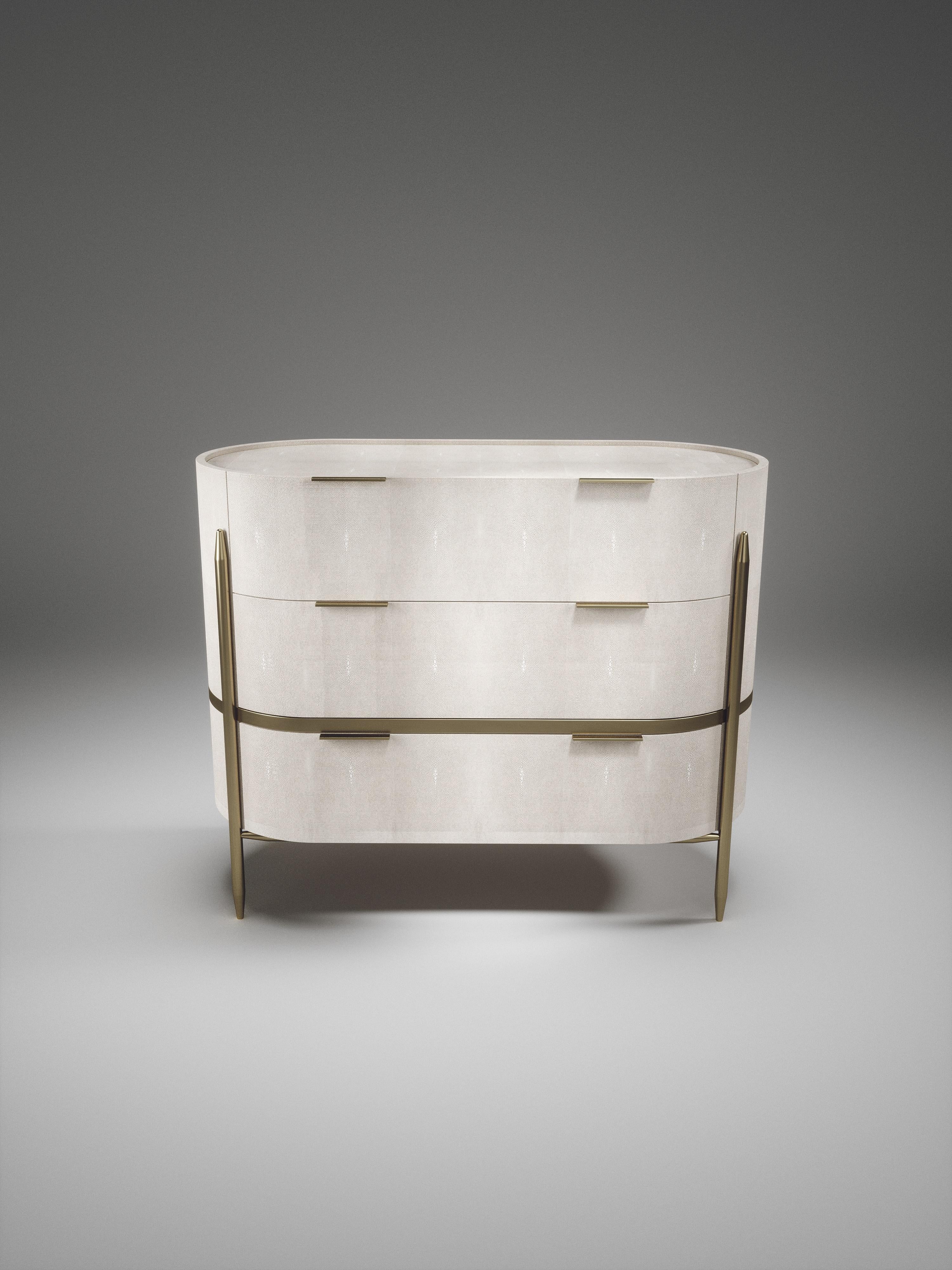 La commode ovale Dandy de Kifu Paris est un accessoire élégant et luxueux, incrusté de galuchat crème et de détails en laiton bronze-patine. Cette pièce comprend 3 tiroirs au total et les intérieurs sont incrustés de placage de bois de gemelina.