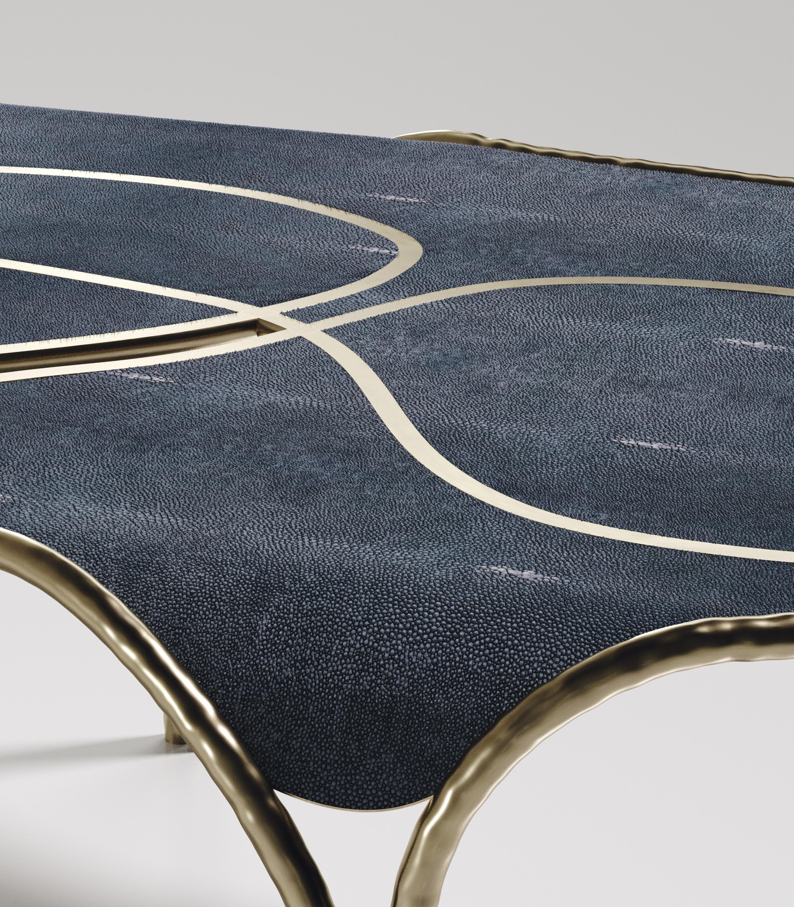 La table basse Arianne de R&Y Augousti est une pièce unique et fantaisiste. L'ensemble de la pièce est incrusté d'un galuchat bleu denim accentué par des détails complexes en laiton bronze-patine qui ont l'effet 