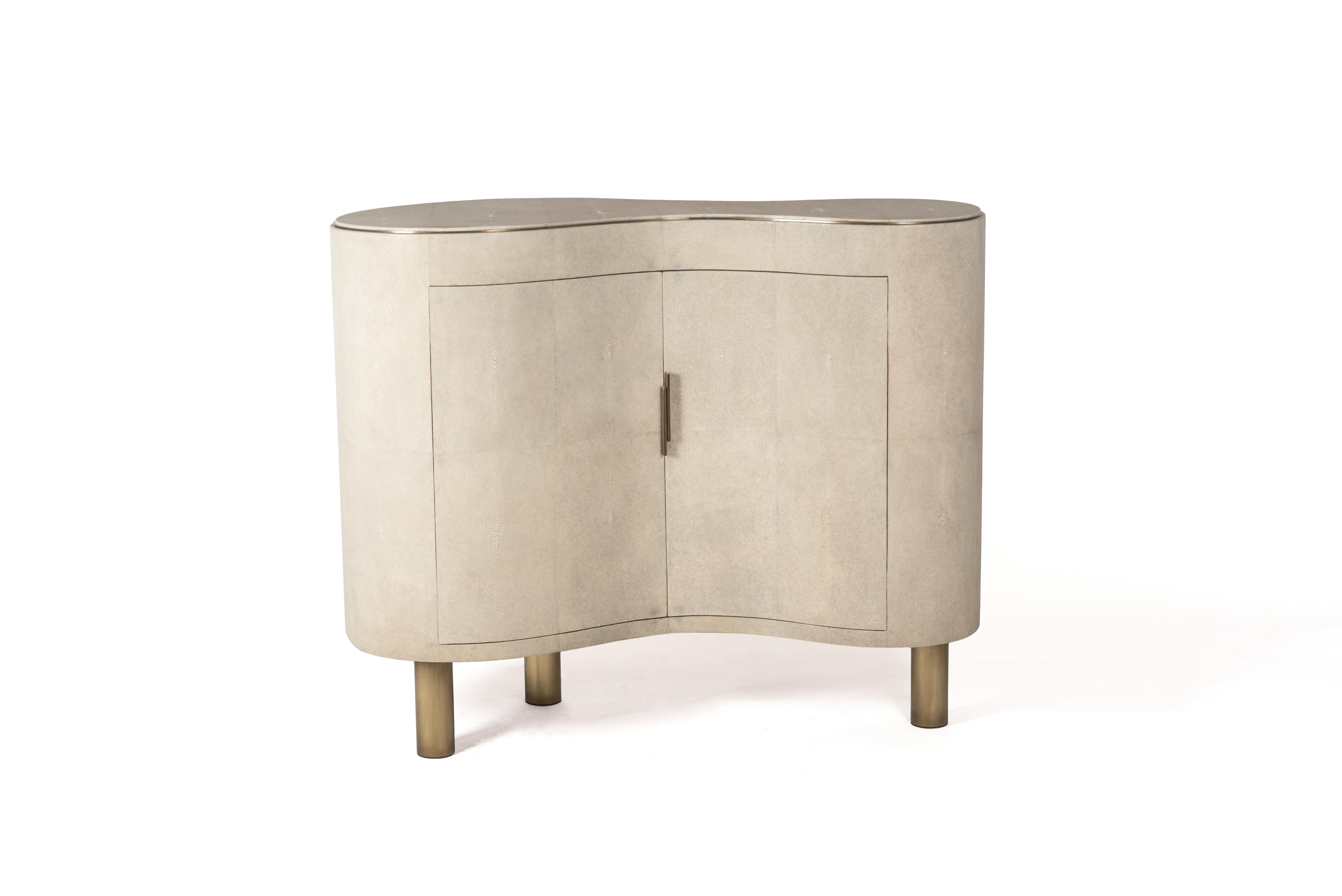 The constellation commode is the perfect storage unit or bar unit for a living room or dining area. The amorphous shaped piece is completely inlaid in cream shagreen. The piece sits on a pair of tubular bronze-patina brass legs. The interior is