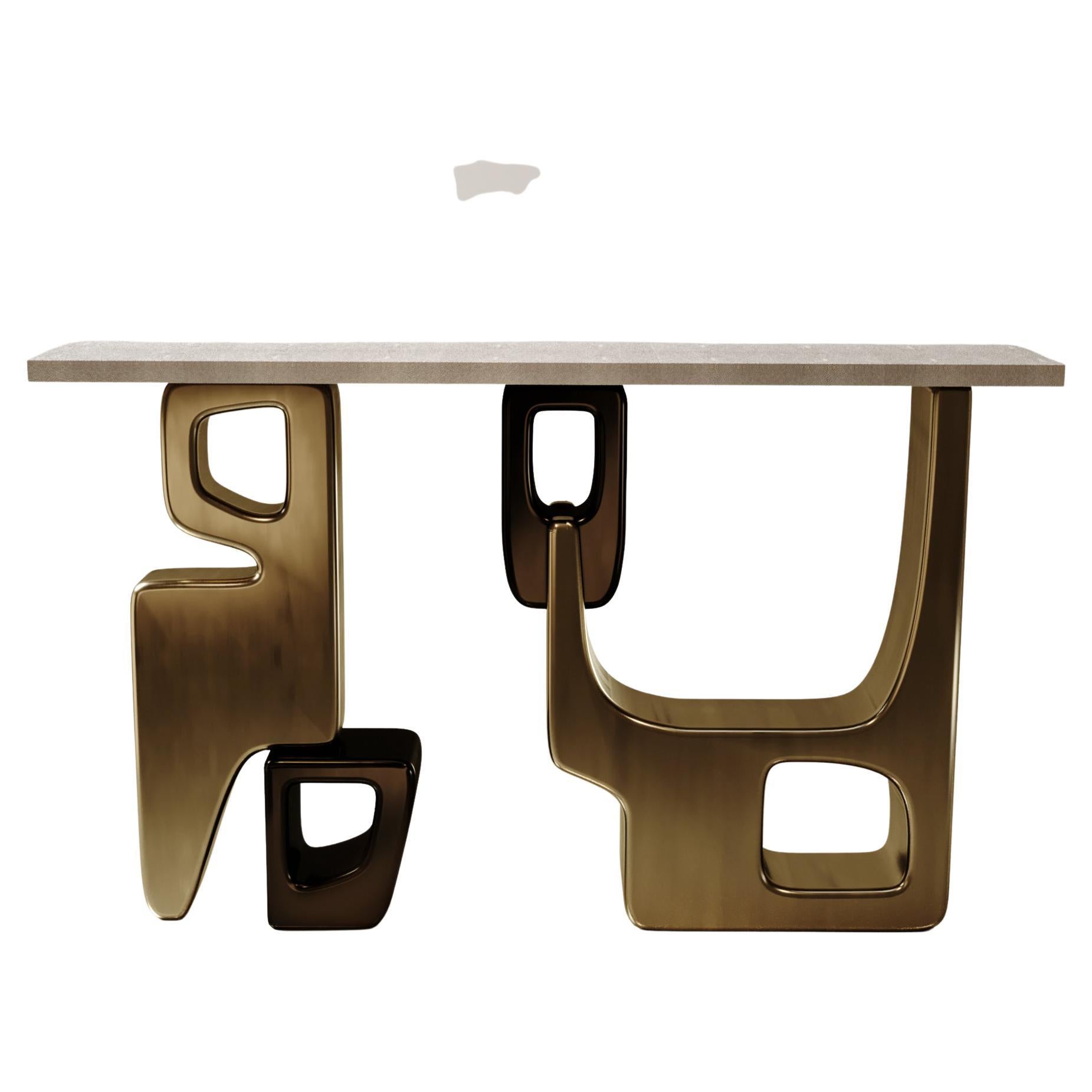 La table console Apoli de Kifu Paris est à la fois spectaculaire et organique grâce à son design unique. Le plateau en marqueterie de galuchat crème repose sur une base géométrique et sculpturale en laiton bronze-patine. Cette pièce a été conçue par