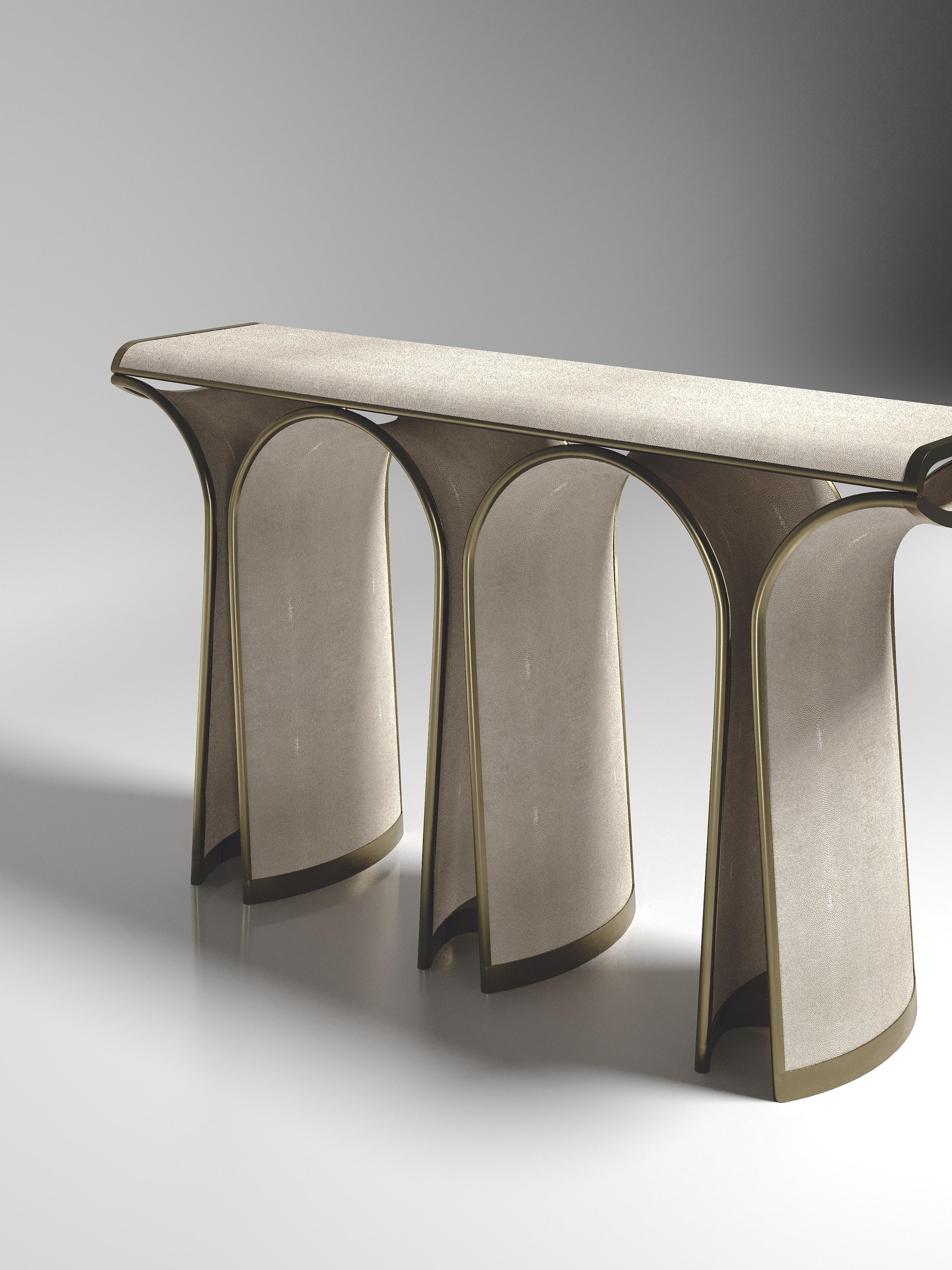 La console Nymphea de R&Y Augousti en galuchat crème avec des détails en laiton bronze-patine explore l'ADN emblématique de la marque, qui consiste à intégrer l'artisanat d'antan dans une ambiance contemporaine et tout à fait luxueuse. Disponible