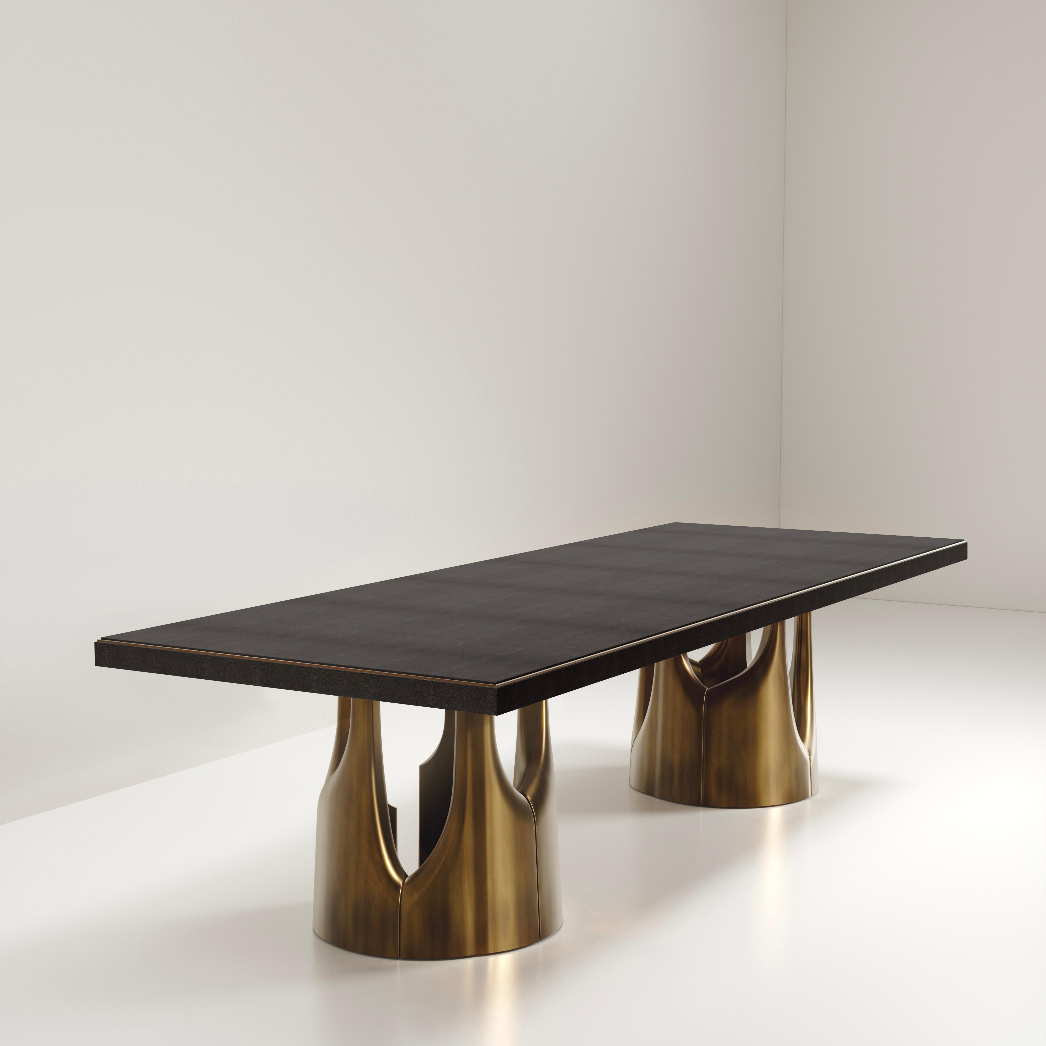 The Triptych I dining table by R&Y Augousti is a stunning multi-faceted sculptural piece. The beautiful hand craved details on the bronze-patina base demonstrate the incredible artisan work of Augousti. The top is inlaid in black shagreen. Available
