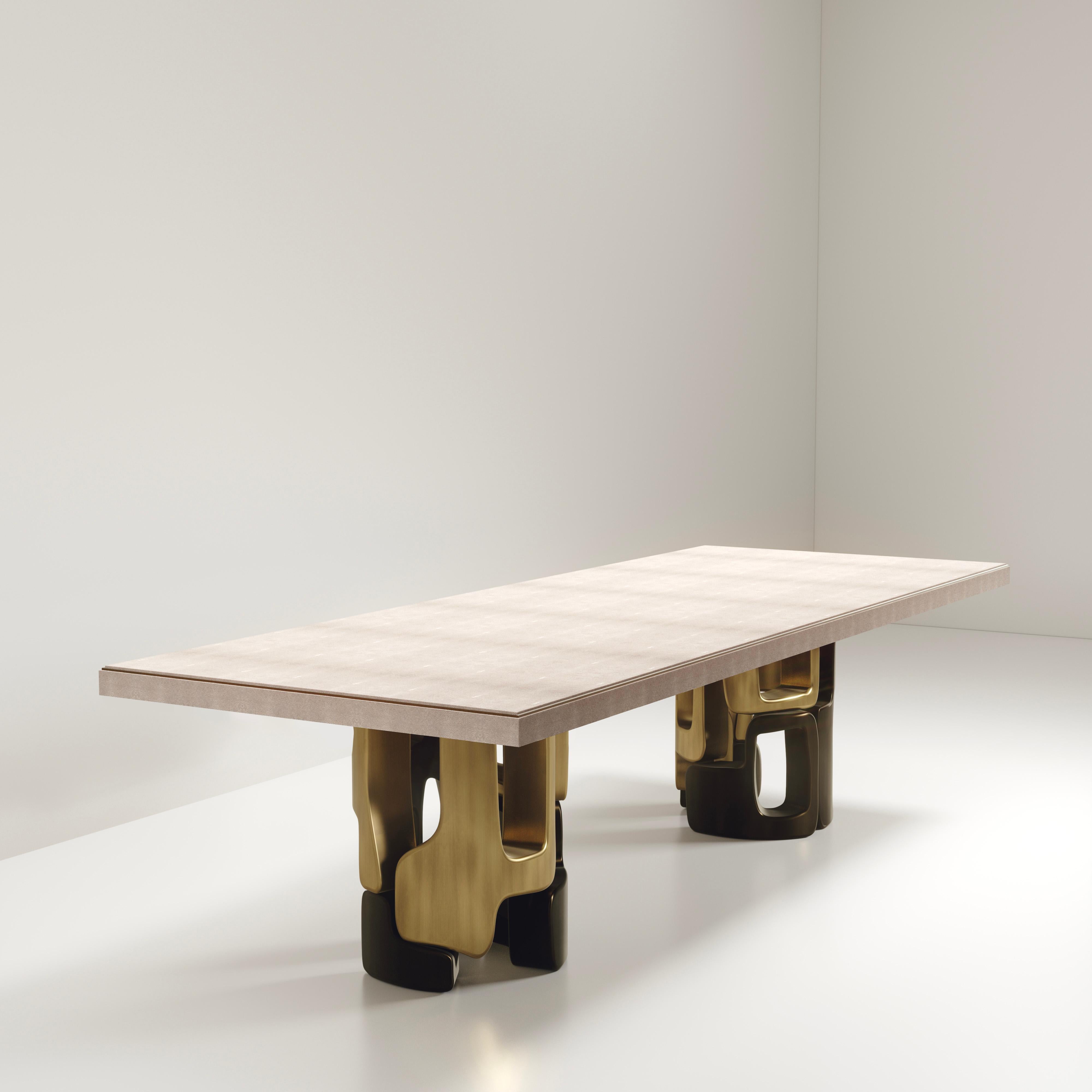 The Apoli I Dining table by Kifu Paris is both dramatic and organic its unique design. The cream shagreen inlaid top sits on a pair of geometric and sculptural bronze-patina brass bases. This piece is designed by Kifu Augousti the daughter of Ria