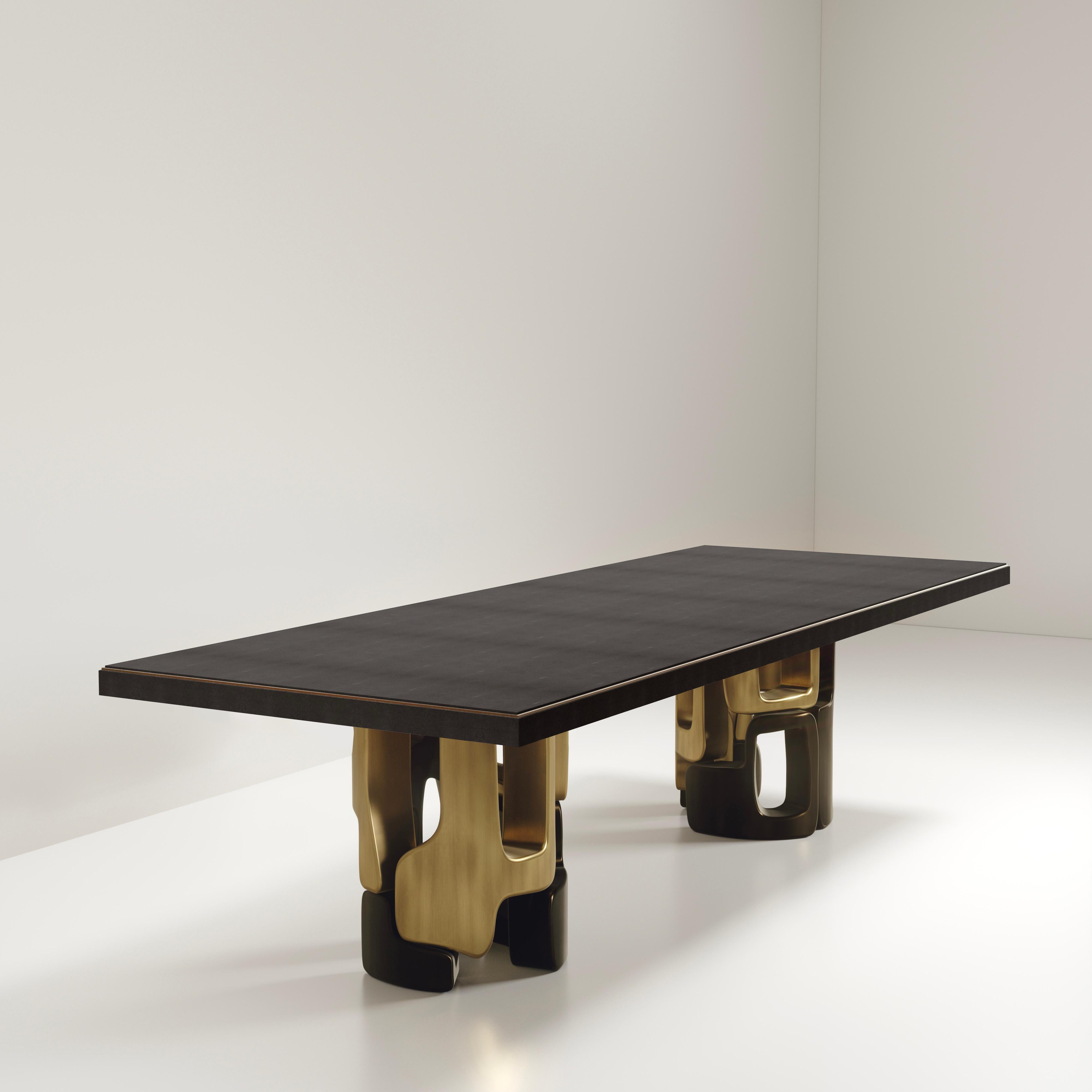 The Apoli I dining table by Kifu Paris is both dramatic and organic its unique design. The black shagreen inlaid top sits on a pair of geometric and sculptural bronze-patina brass bases. This piece is designed by Kifu Augousti the daughter of Ria