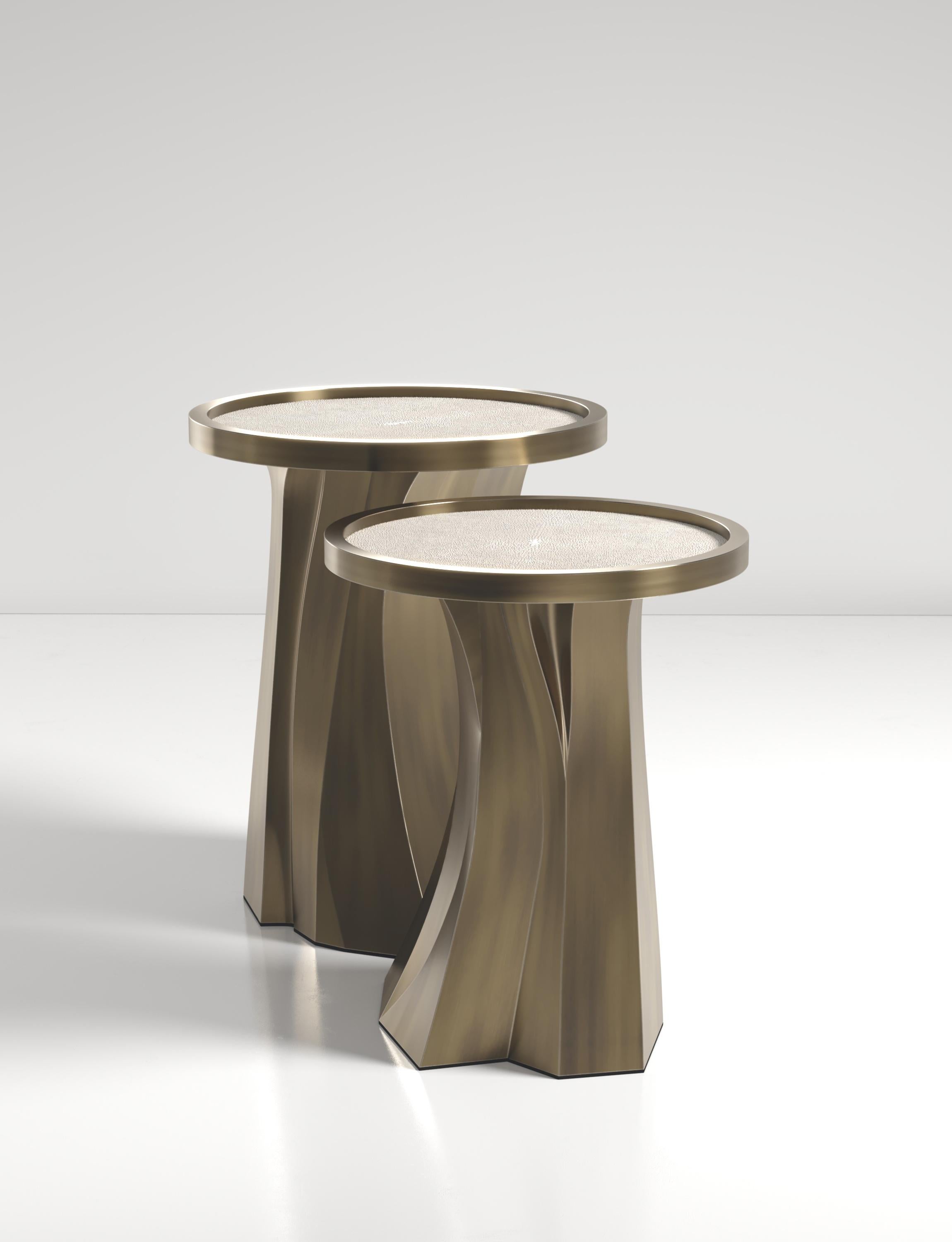 Die Alma Nesting Tables von R&Y Augousti sind skulpturale und vielseitige Stücke. Die cremefarbene Chagrin-Intarsienplatte geht in einen dramatischen, handgeschnitzten Sockel aus Bronze-Patina über. Die Rillen und Details auf der Basis ermöglichen