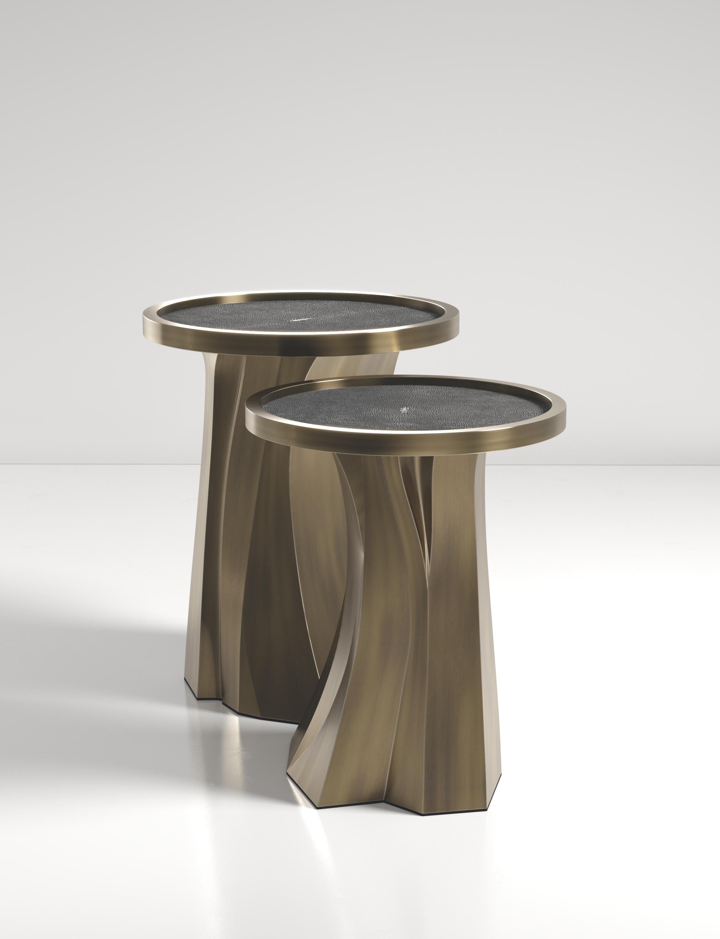 Die Alma Nesting Tables von R&Y Augousti sind skulpturale und vielseitige Stücke. Die mit kohlschwarzem Chagrin eingelegte Platte geht in einen dramatischen, handgeschnitzten Sockel aus Bronze-Patina über. Die Rillen und Details auf der Basis