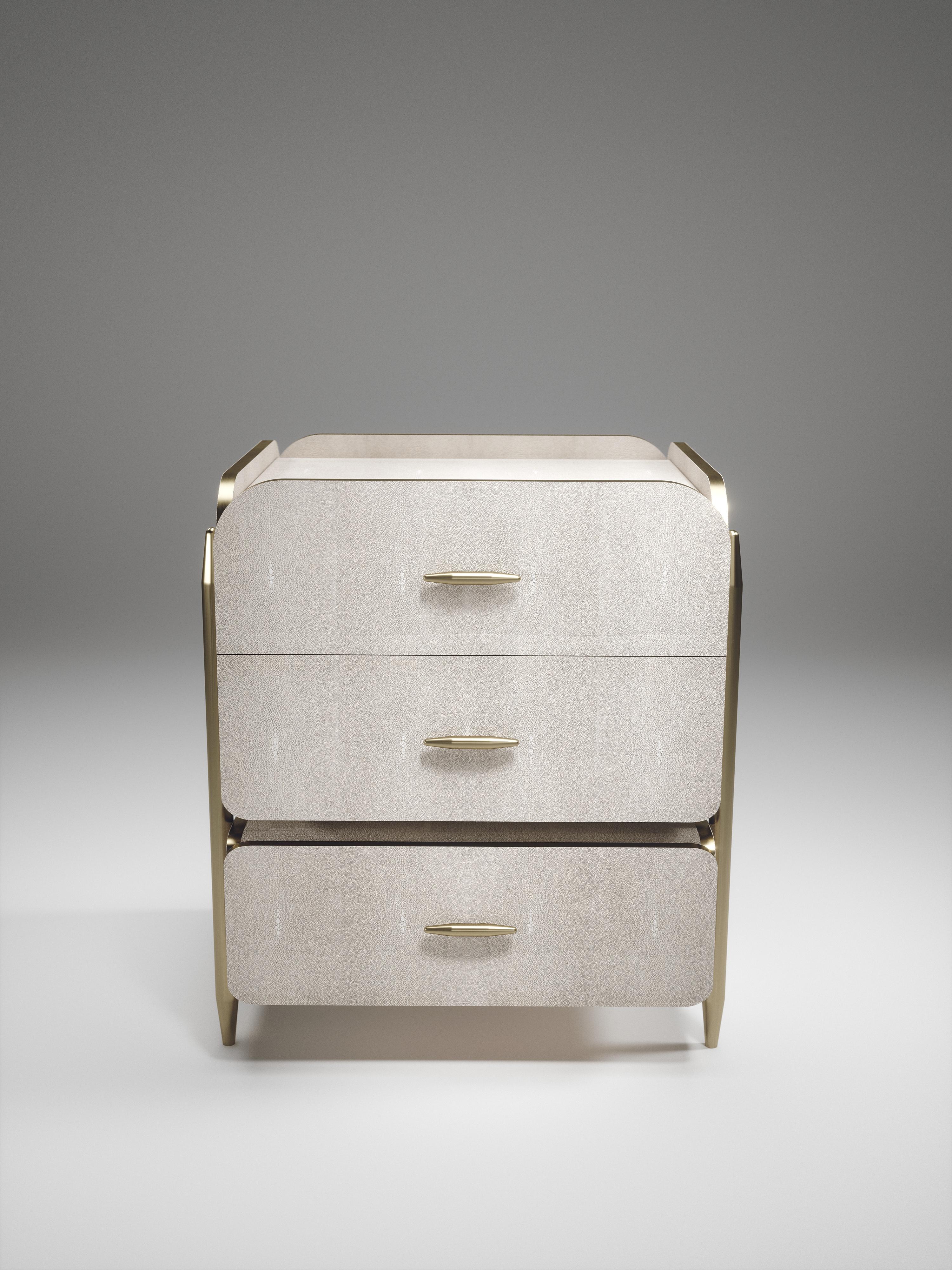 The Dandy square bedside table by Kifu Paris is an elegant and luxurious home accent, inlaid in cream shagreen with bronze-patina brass details. This piece includes 3 drawers total and the interiors are inlaid in gemelina wood veneer. This piece is