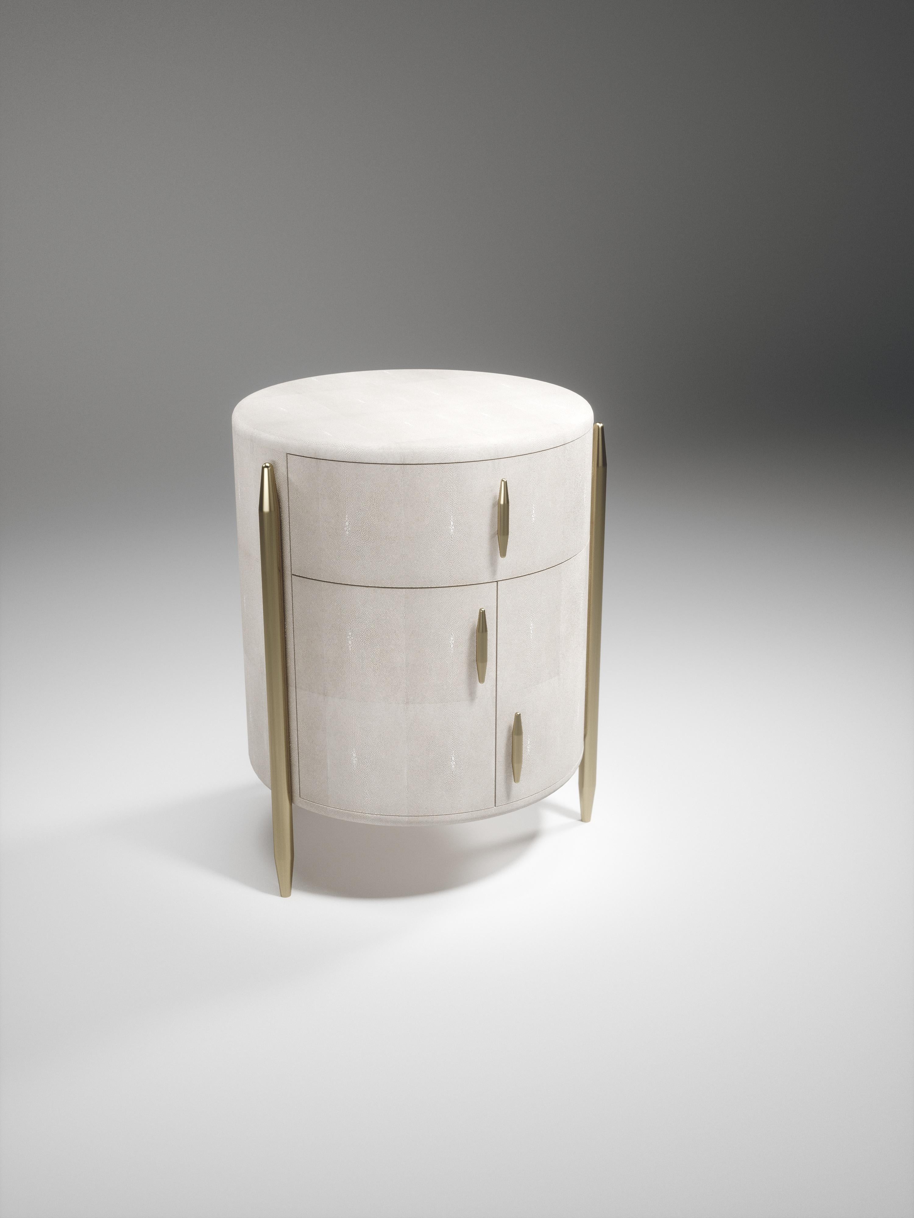 The Dandy round bedside table by Kifu Paris is an elegant and a luxurious home accent, inlaid in cream shagreen with bronze-patina brass details. This piece includes 1 drawer total and a cabinet below; the interiors are inlaid in gemelina wood