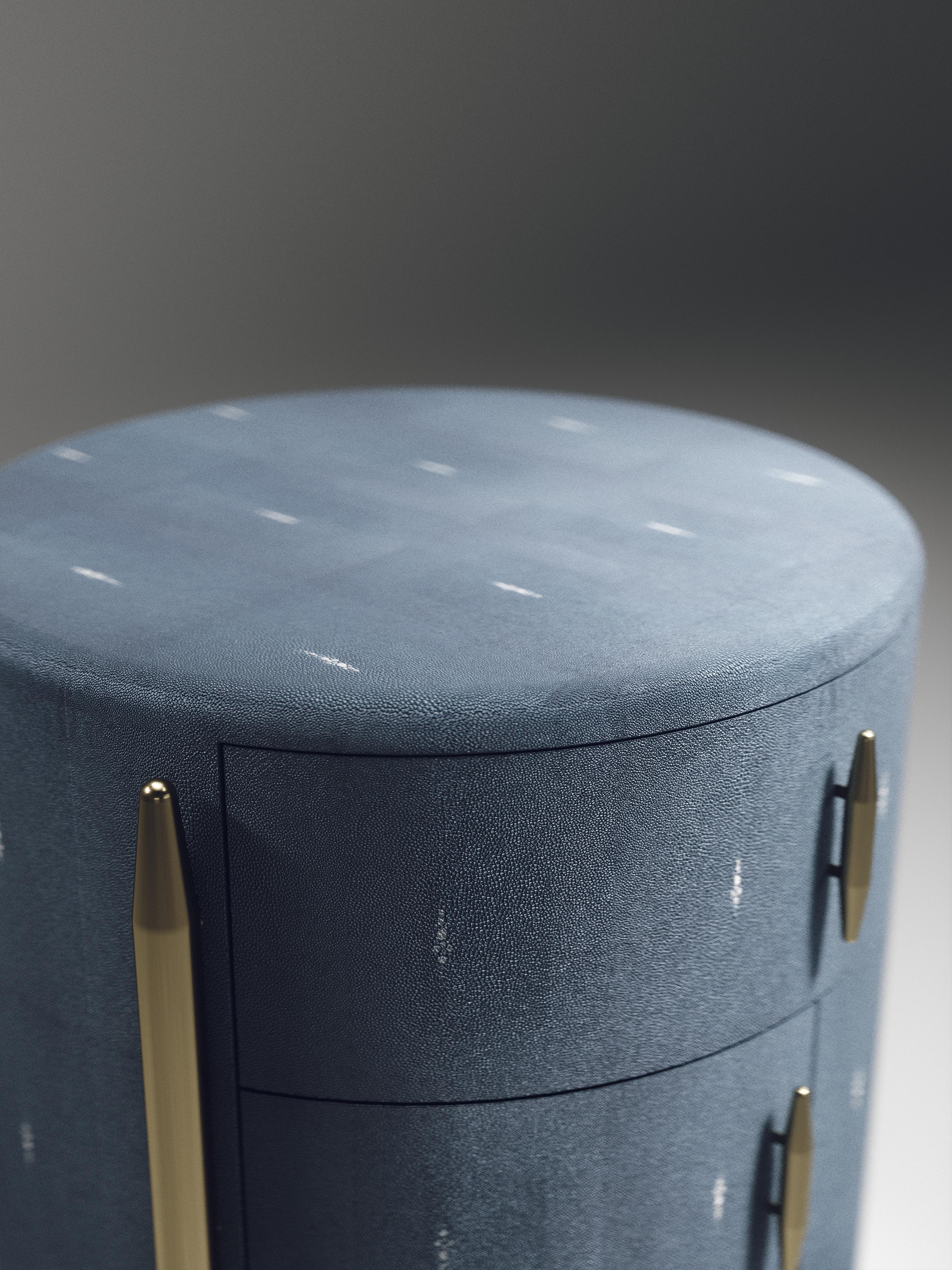The Dandy round bedside table by Kifu Paris is an elegant and a luxurious home accent, inlaid in dark denim blue shagreen with bronze-patina brass details. This piece includes 1 drawer total and a cabinet below; the interiors are inlaid in gemelina
