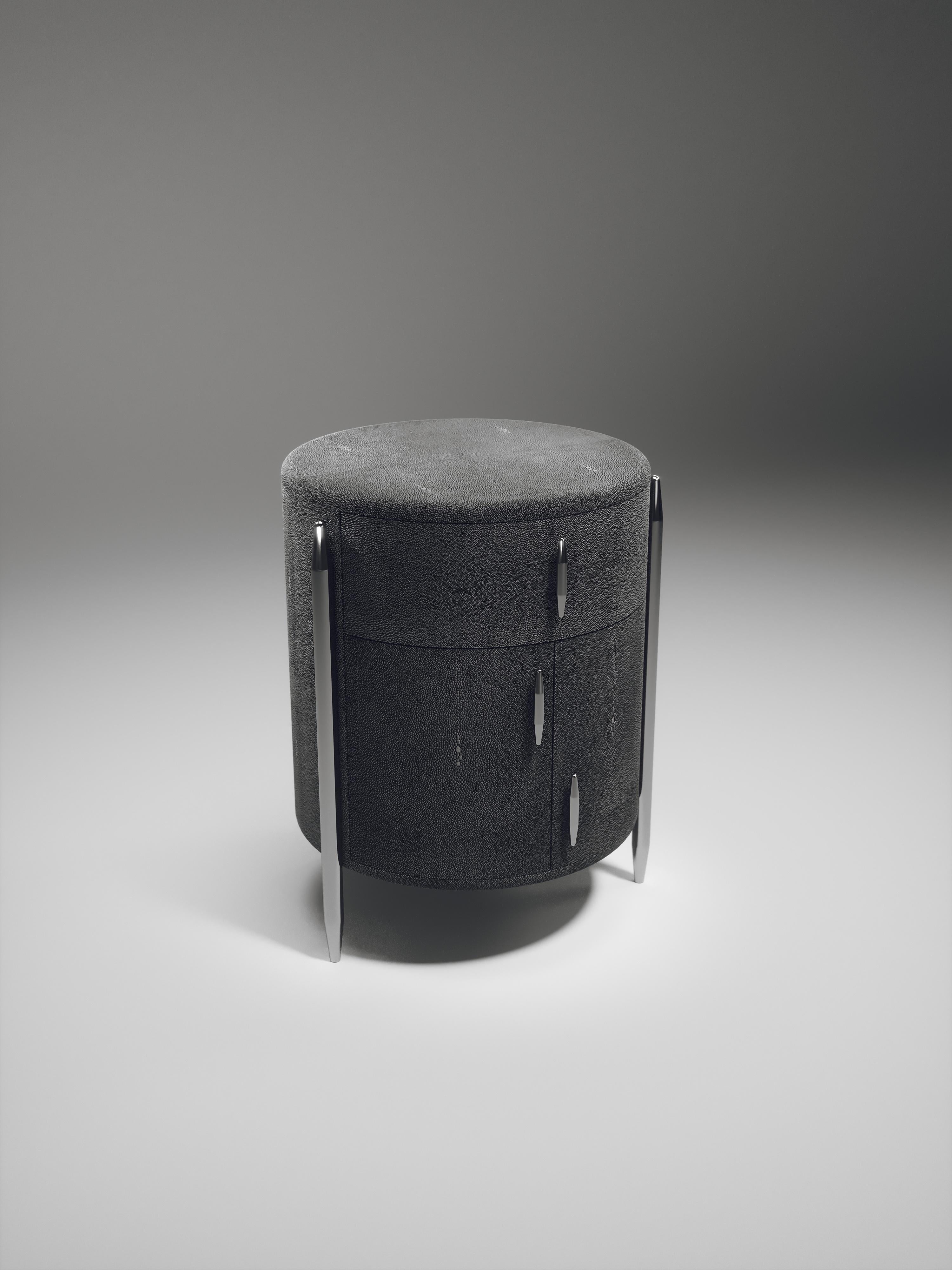 The Dandy round bedside table by Kifu Paris is an elegant and a luxurious home accent, inlaid in black shagreen with polished stainless steel details. This piece includes 1 drawer total and a cabinet below; the interiors are inlaid in gemelina wood