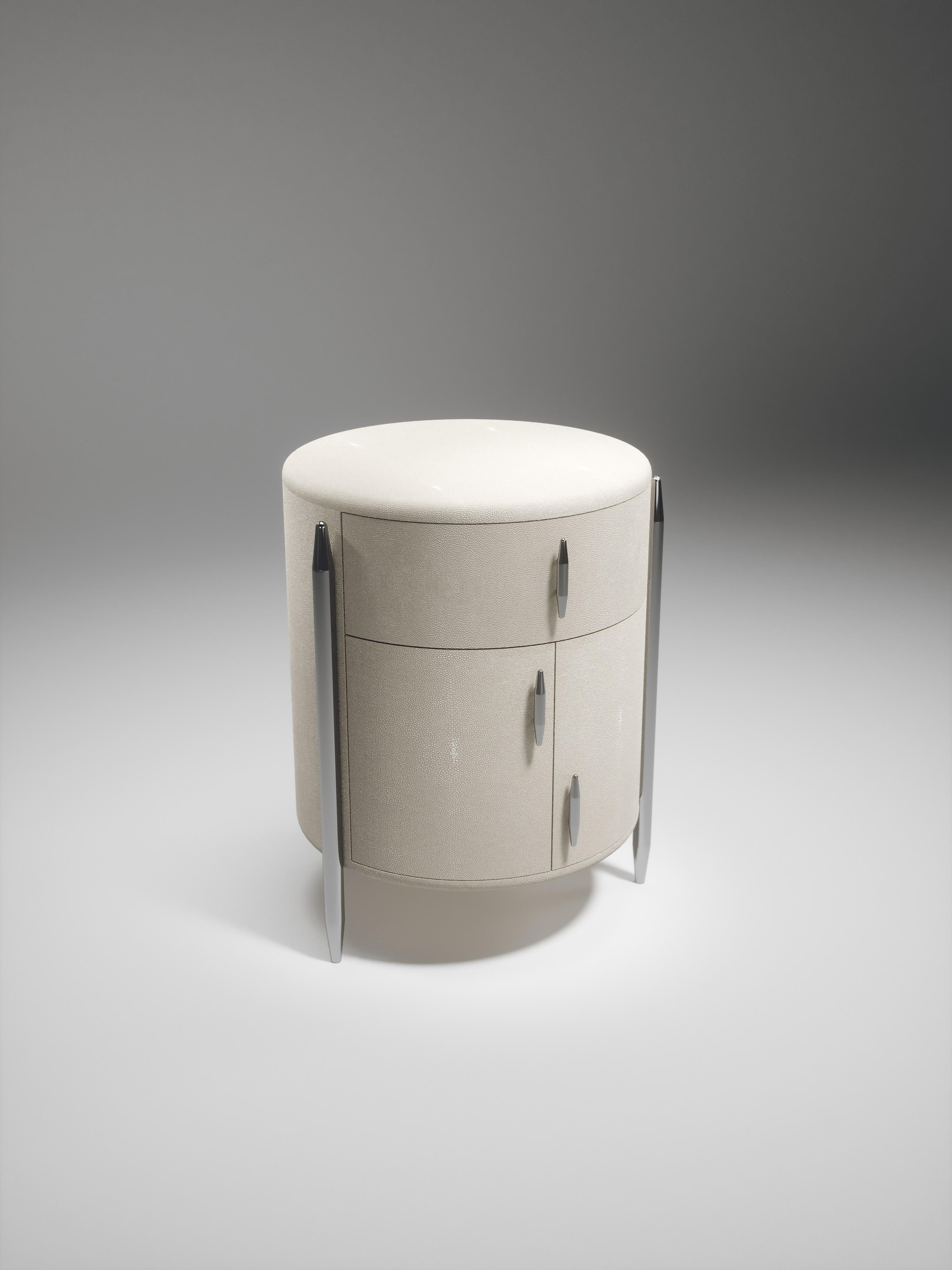 The Dandy round bedside table by Kifu Paris is an elegant and a luxurious home accent, inlaid in cream shagreen with polished stainless steel details. This piece includes 1 drawer total and a cabinet below; the interiors are inlaid in gemelina wood
