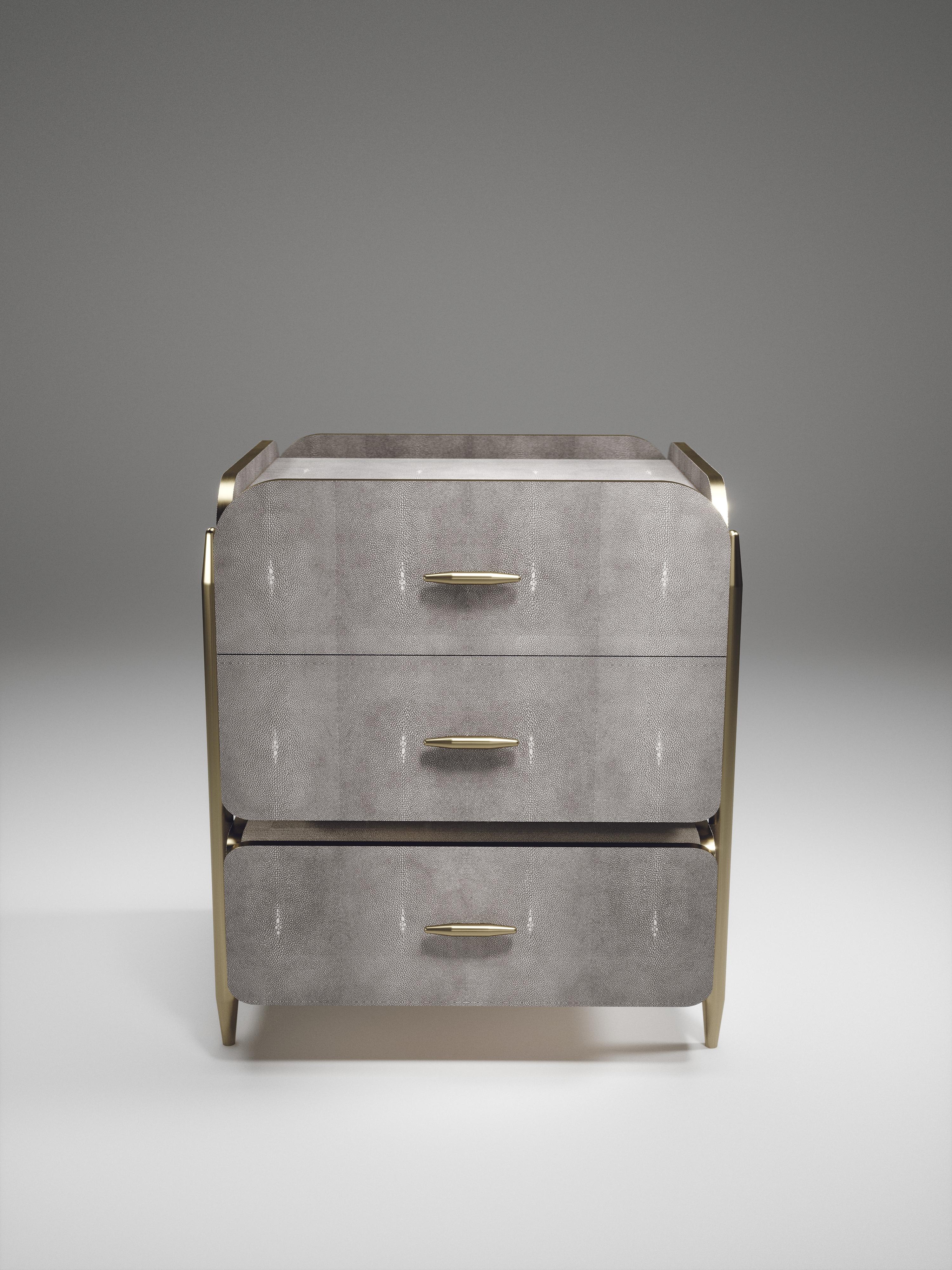 The Dandy Square Bedside Table by Kifu Paris is an elegant and a luxurious home accent, inlaid in light grey shagreen with bronze-patina brass details. This piece includes 3 drawers total and the interiors are inlaid in gemelina wood veneer.