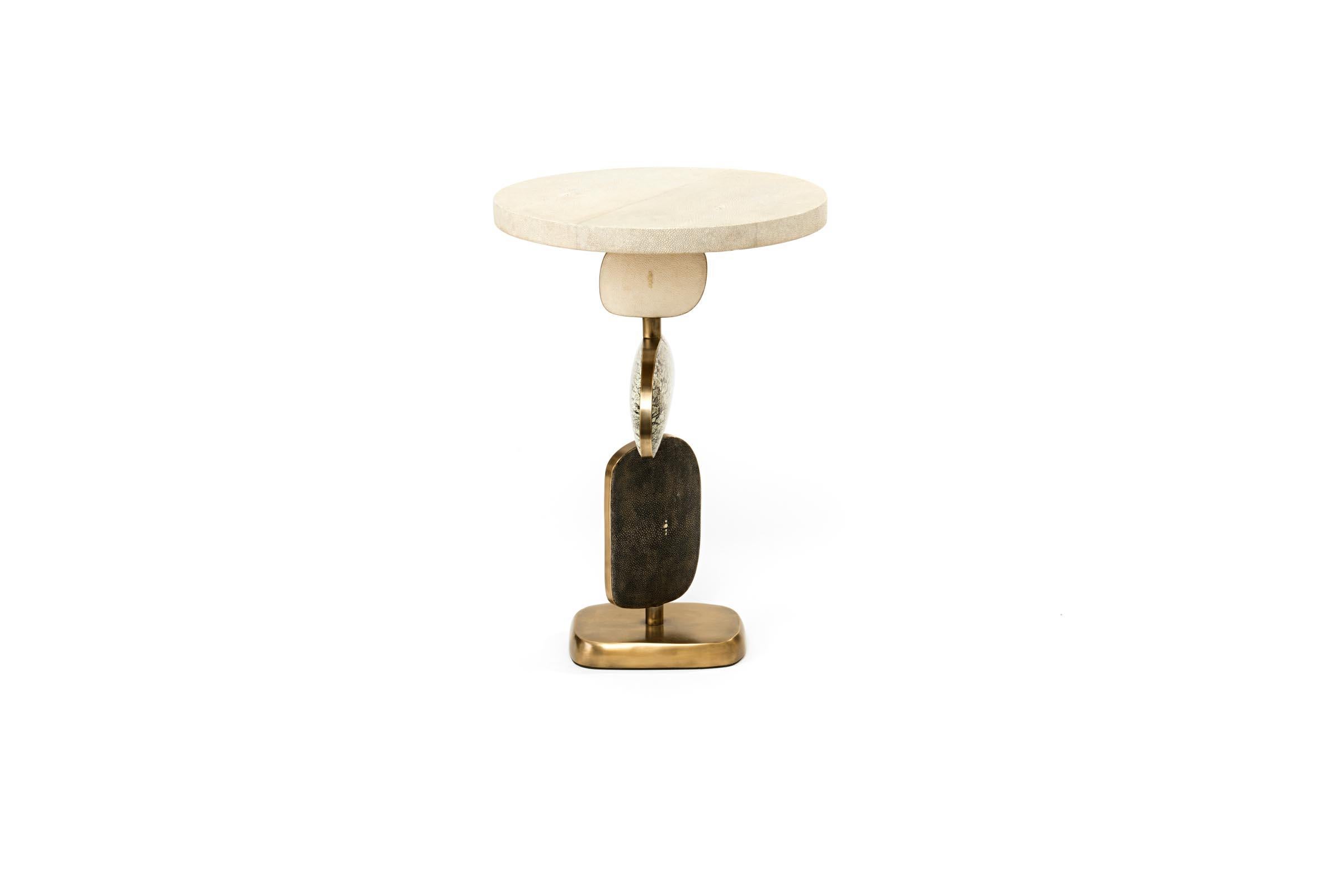 La table d'appoint Cosmo de Kifu Paris est une pièce fantaisiste et sculpturale, incrustée de galuchat crème/galuchat noir réversible, de pierre de Baguio, de coquille de stylo noire et de laiton bronze-patina. Les formes amorphes de la partie