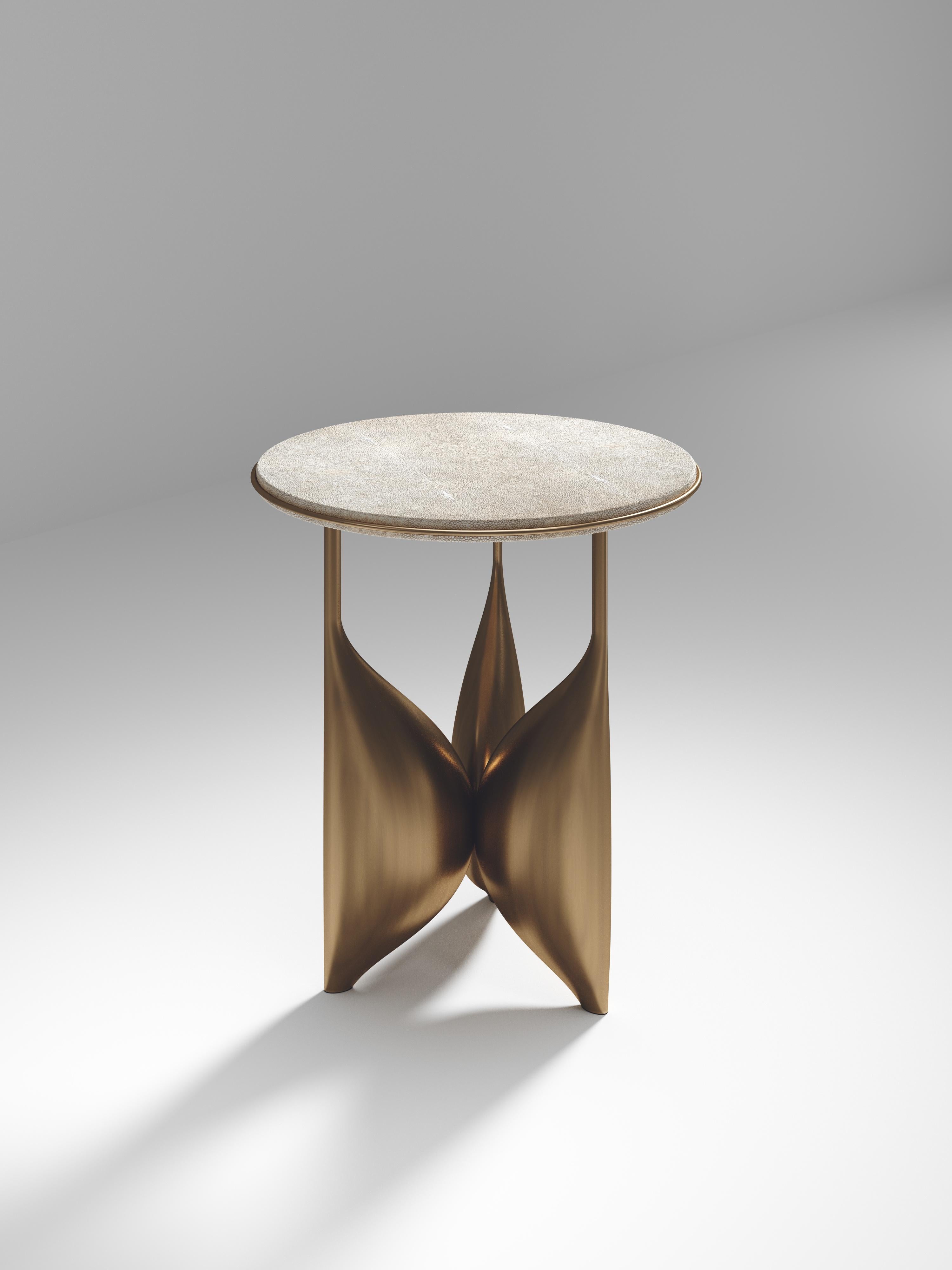 The Plumeria side table II by Kifu Paris is a dramatic and sculptural piece. The cream shagreen inlaid top sits on a sculptural bronze-patina brass base that is conceptually inspired by bird feathers floating on top of a lake. The border of the top
