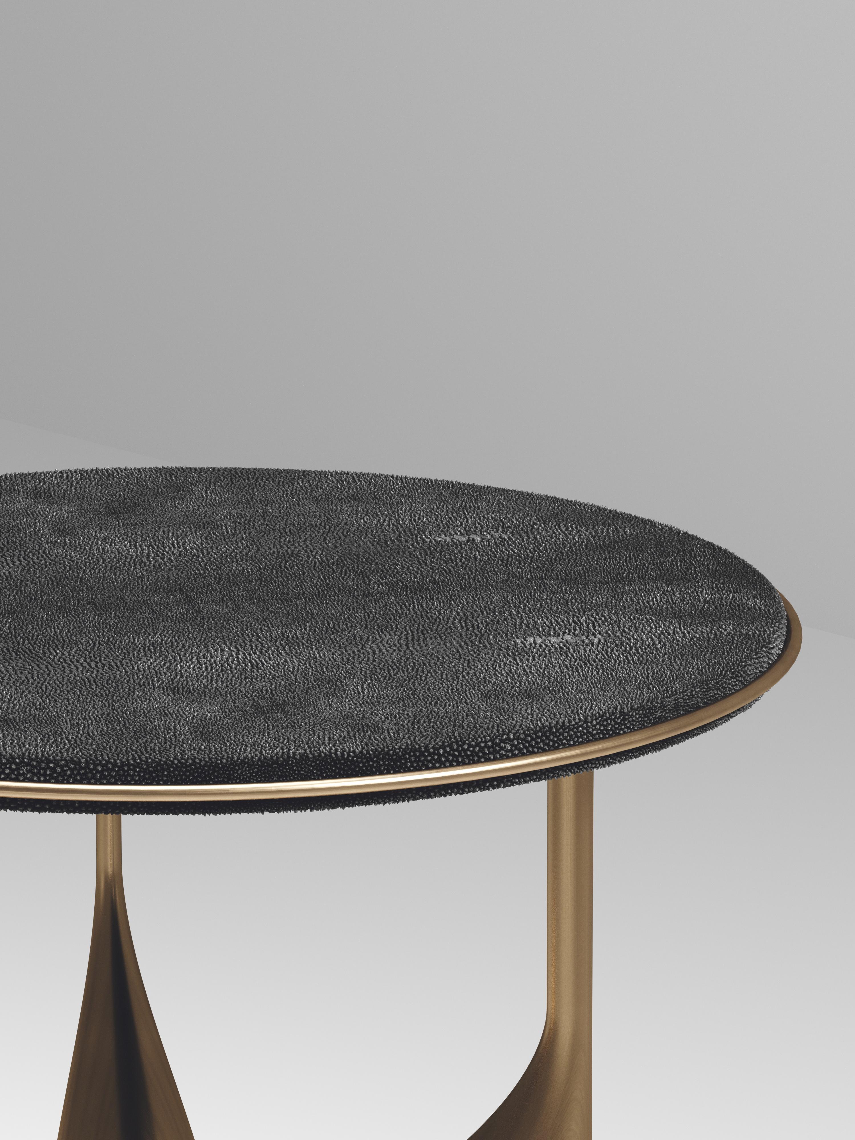 The Plumeria Side Table II by Kifu Paris is a dramatic and sculptural piece. The coal black shagreen inlaid top sits on a sculptural bronze-patina brass base that is conceptually inspired by bird feathers floating on top of a lake. The border of the