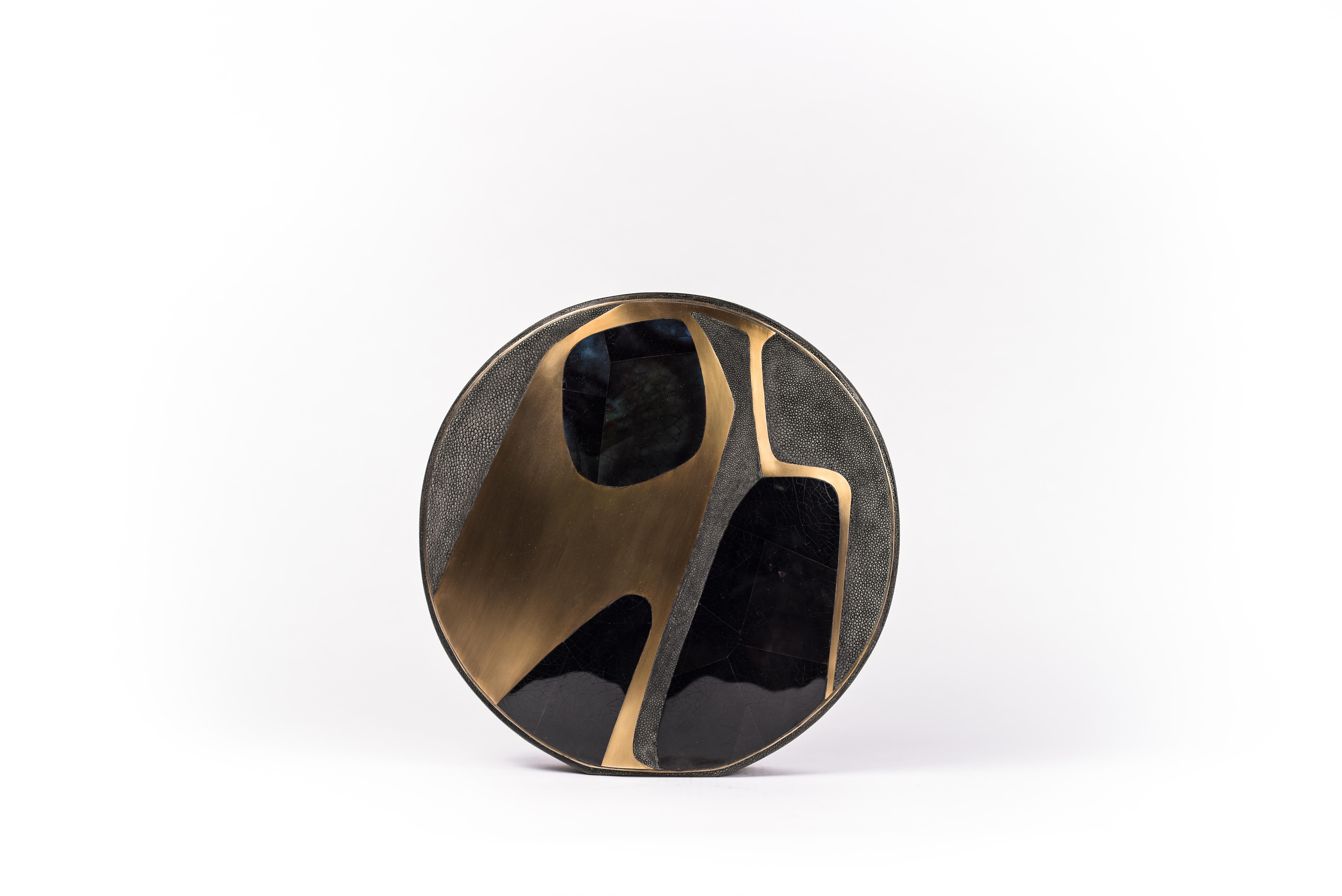 The Cosmos circular vase is a graphic piece that adds a statement to any space. The bold pattern is inlaid in a mixture of coal black shagreen, blue pen shell and bronze-patina brass. The circular vase has a metal indentation around it and is lined