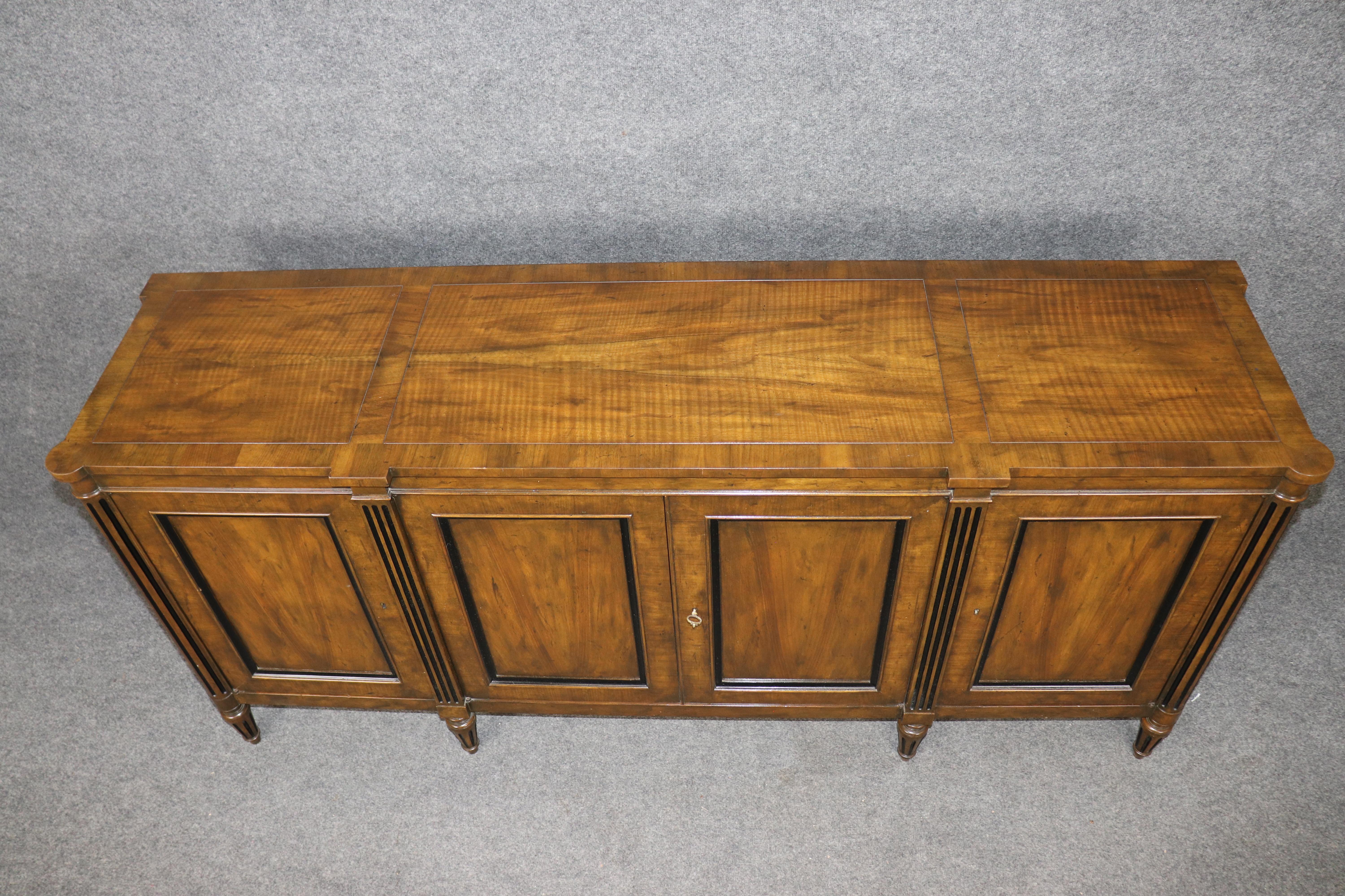 Elevate your home with this timeless Baker Furniture Company French Directoire Style Sideboard, expertly crafted in rich fiddle-back walnut. A distinguished example of Baker’s commitment to heirloom-quality design, this sideboard features four