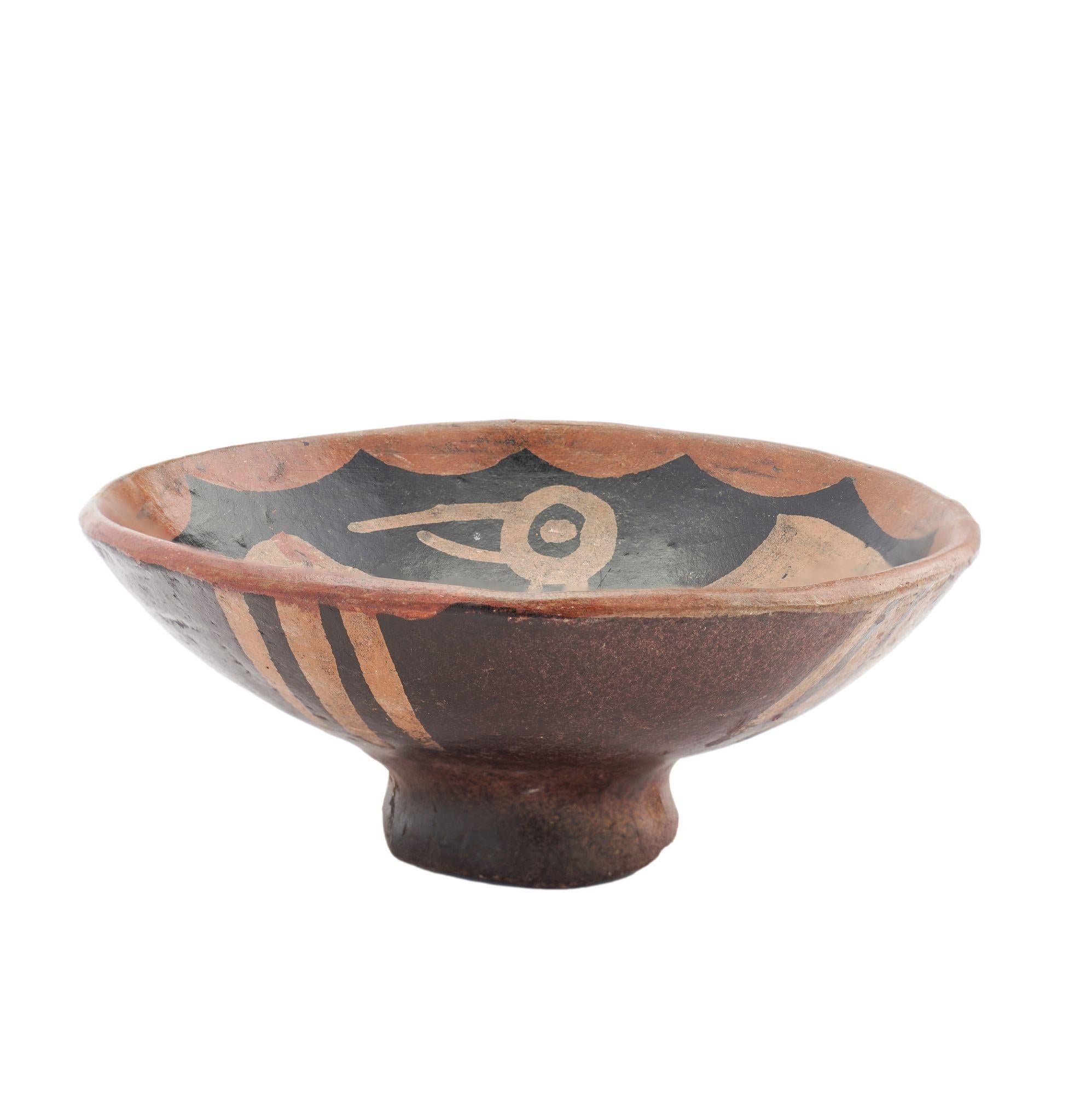 Hand thrown shallow footed pottery bowl decorated after a Pre-Columbian model. The design centers on a single bird with outstretched wings, surrounded by a scalloped boarder along the rim. The underside is decorated with three parallel lines at the