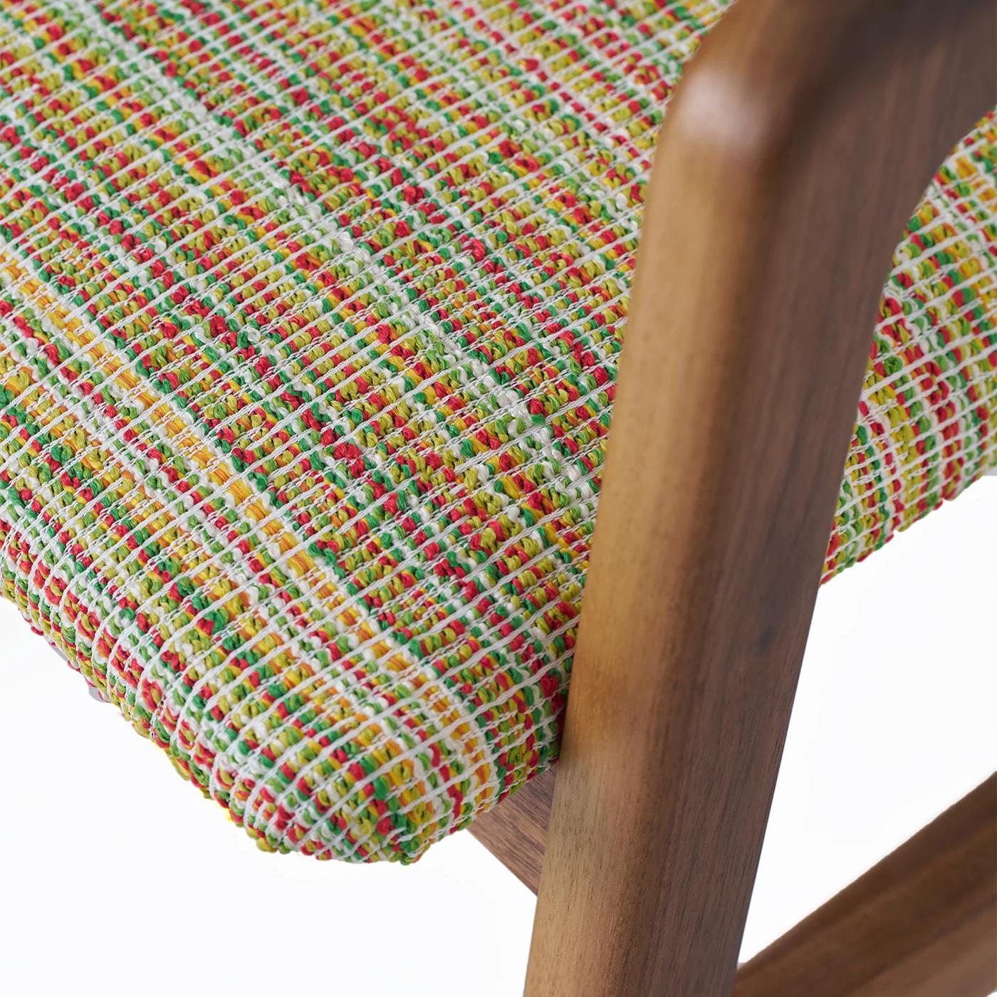 Una silla de tamaño medio con armazón de nogal macizo y acabado al aceite, diseñada para resaltar el veteado natural y la durabilidad de la madera. El asiento y el respaldo están recubiertos de tejido técnico con un estampado multicolor que añade
