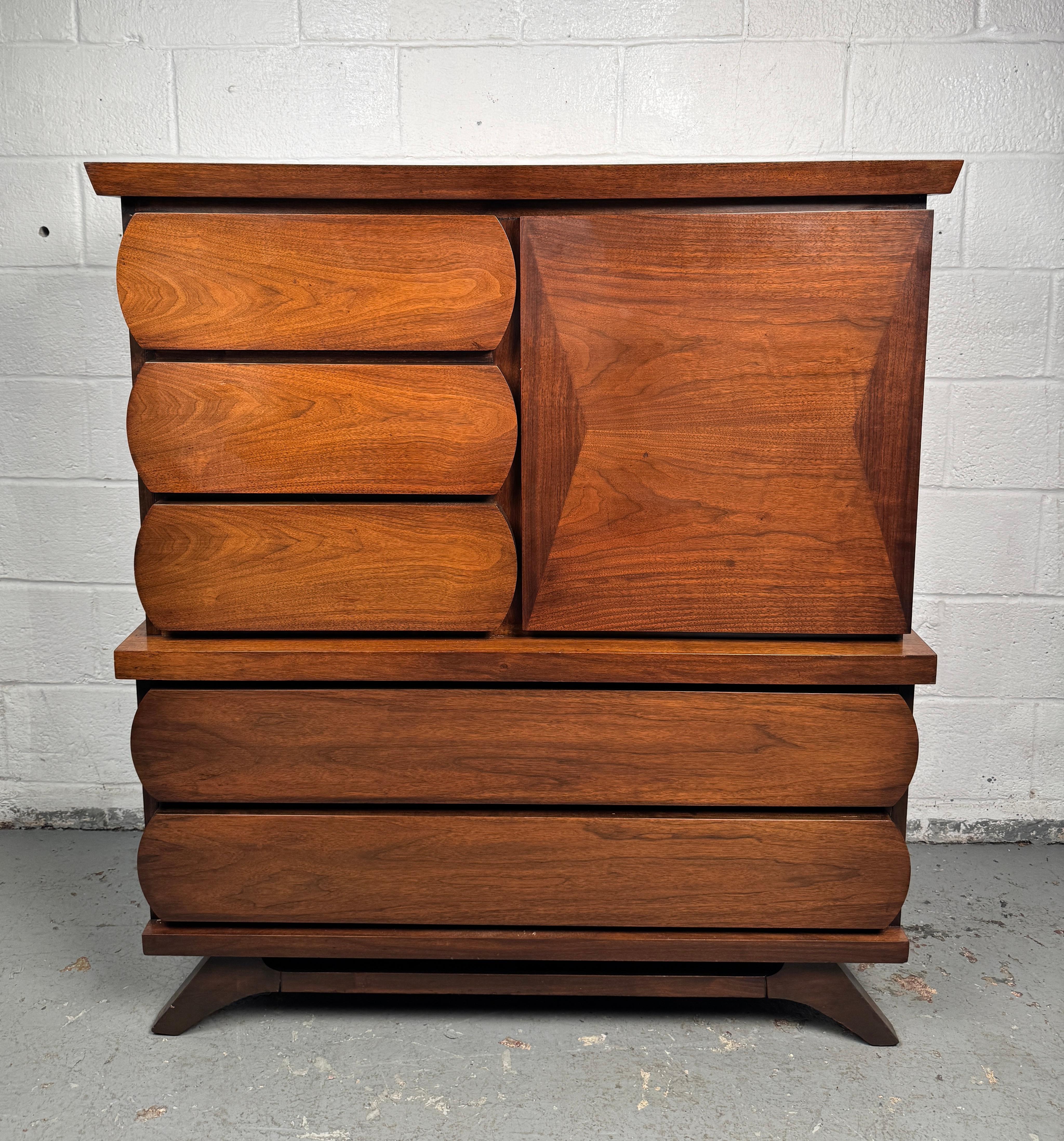 Striking mid-century highboy dresser crafted in walnut, featuring a sculptural silhouette and a distinctive 1960s-style facade. Designed with ample storage and bold geometric details, this piece captures the era’s playful yet sophisticated