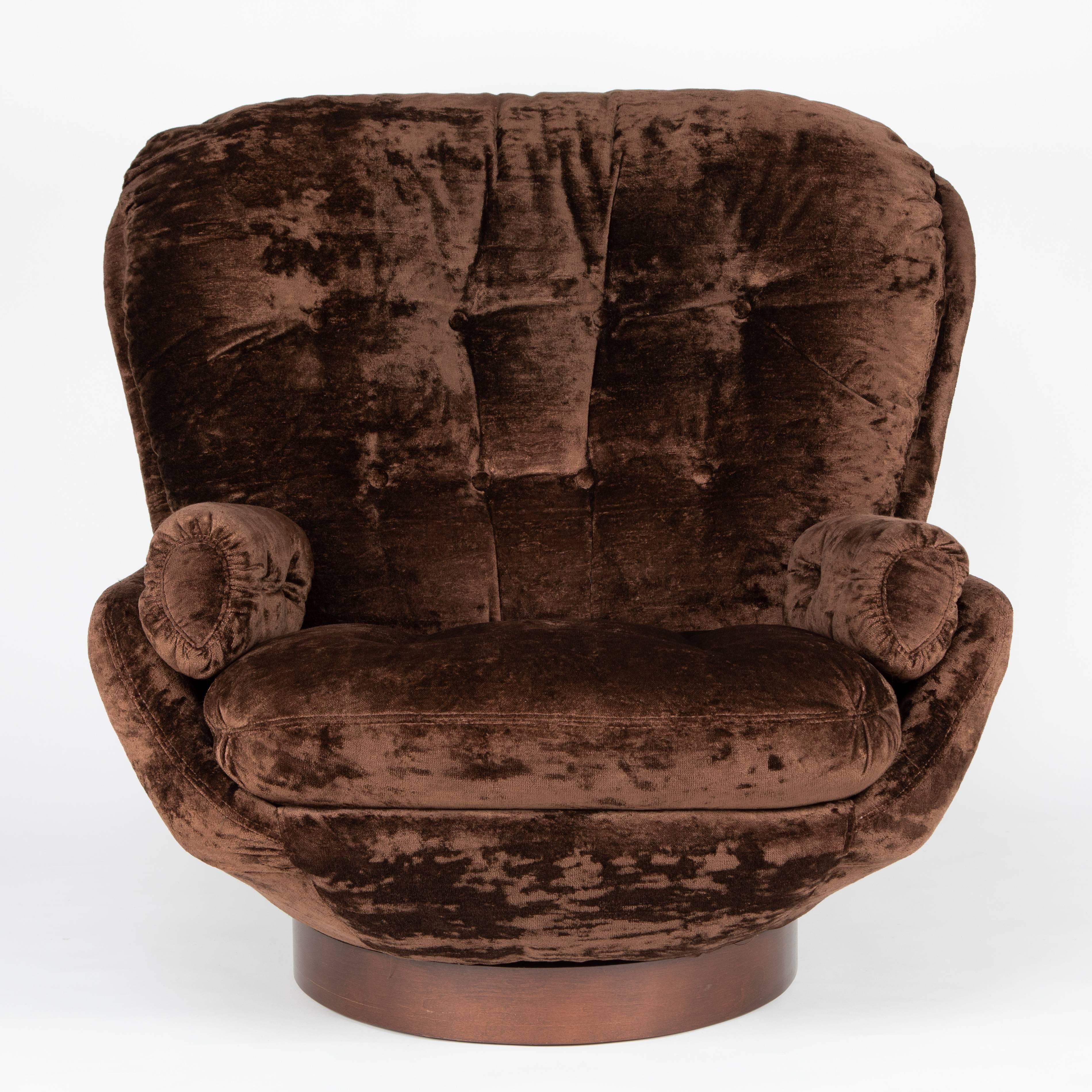 Large and curvaceous lounge chair and ottoman in original chocolate-brown crushed velvet. The back cushion is fixed; the loose seat cushion is flanked by fixed arm cushions; all are button-tufted. The chair and ottoman rest on walnut-wrapped,