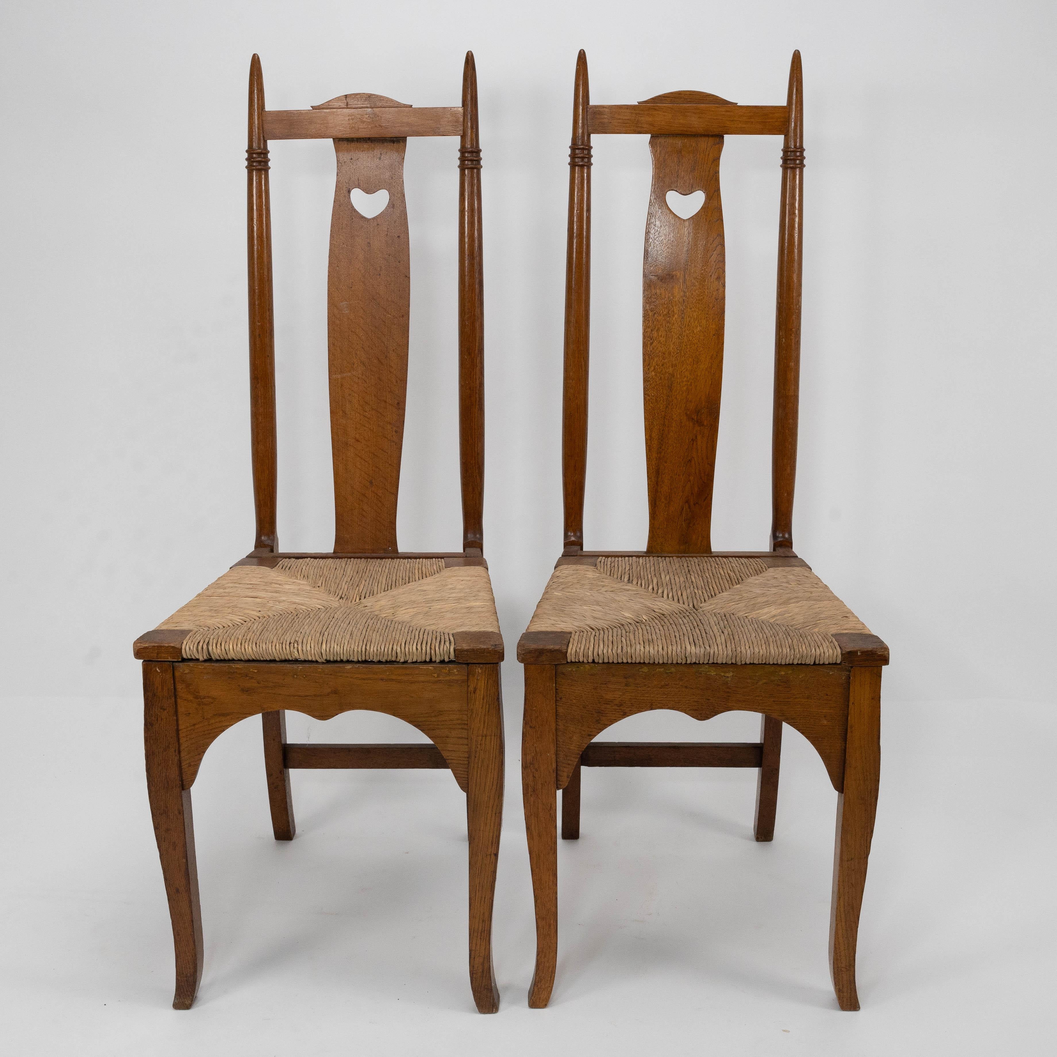 Shapland & Petter. A pair of Arts & Crafts oak dining or side chairs in the style of George Walton with finely turned tops, pierced hearts to the backs with lower arched aprons and Queen Anne style legs. 
Both rush seats have been professionally re
