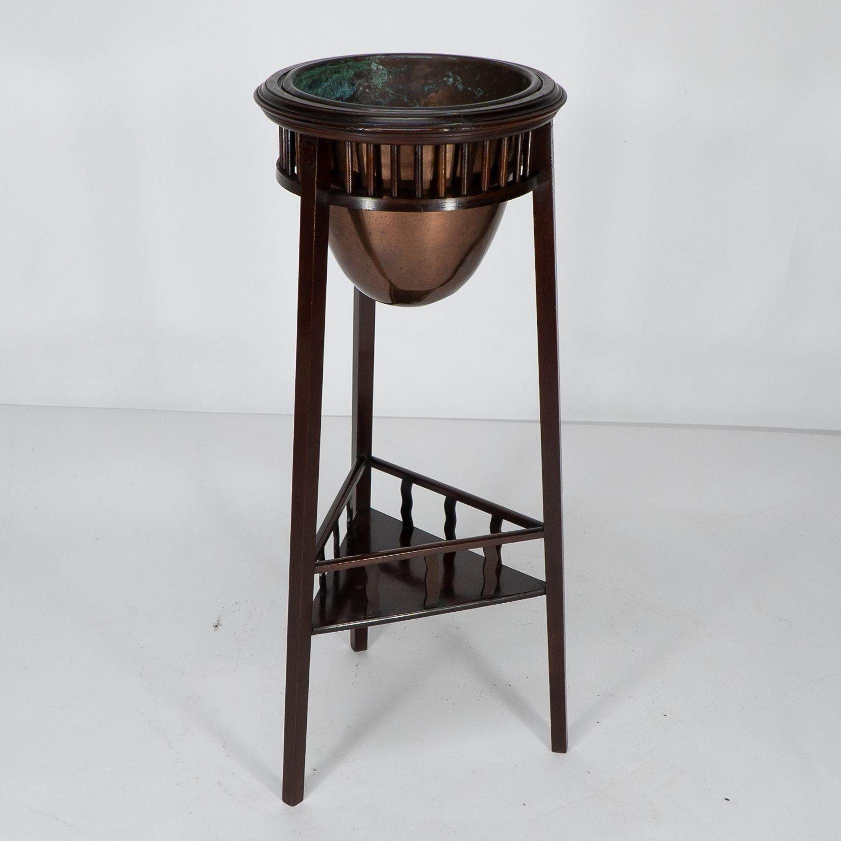 Shapland et Petter. Rare cache-pot Arts and Crafts à deux niveaux en noyer à trois pieds, le tablier supérieur avec une rangée de tournures incisées et le pot de fleurs en cuivre d'origine de bonne qualité. La tablette inférieure triangulaire avec