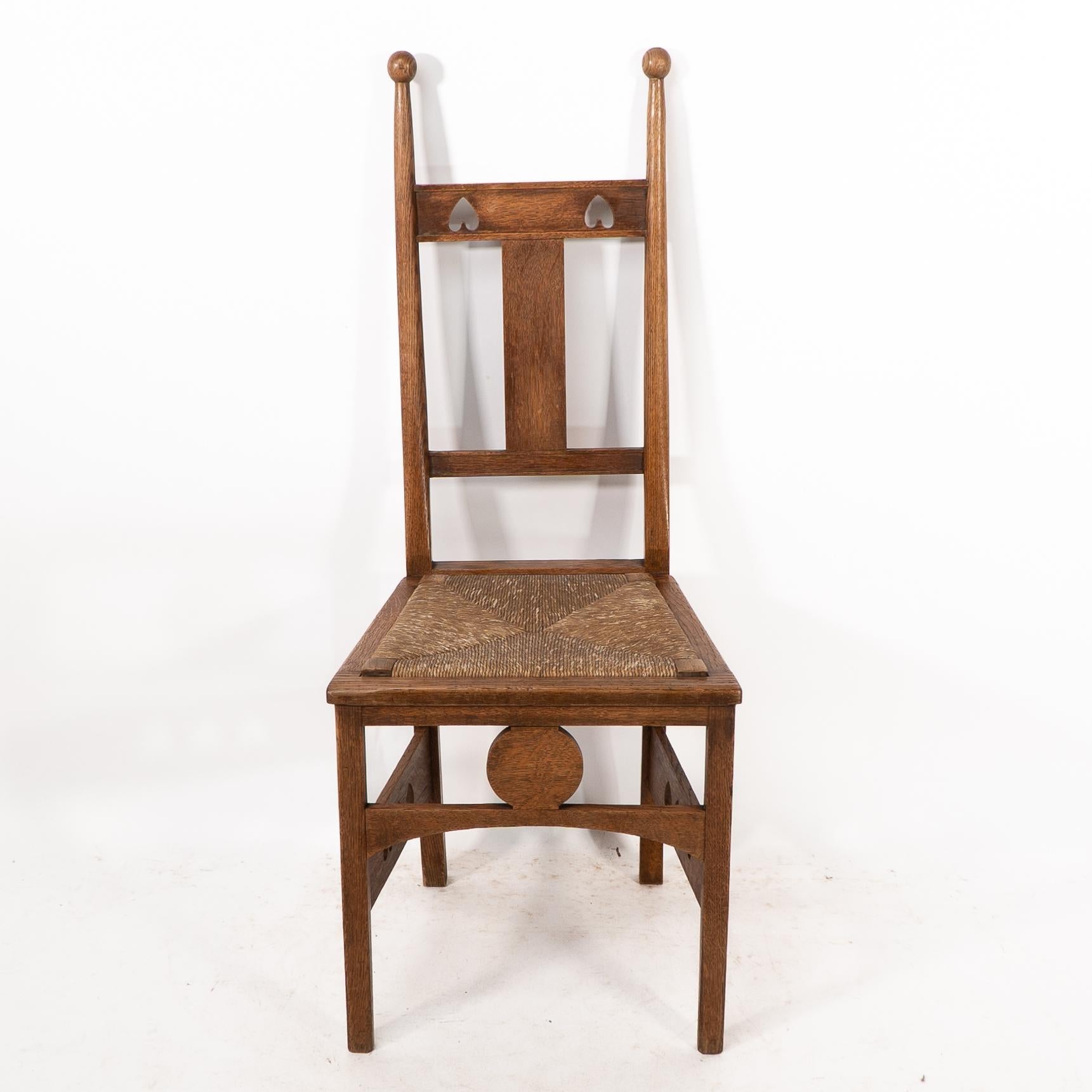 Shapland and Petter. An Arts and Crafts oak desk or side chair with ball finials and pierced hearts to the head rest and to the wide side stretchers with a circular motif to the front stretcher and the original rush seat.