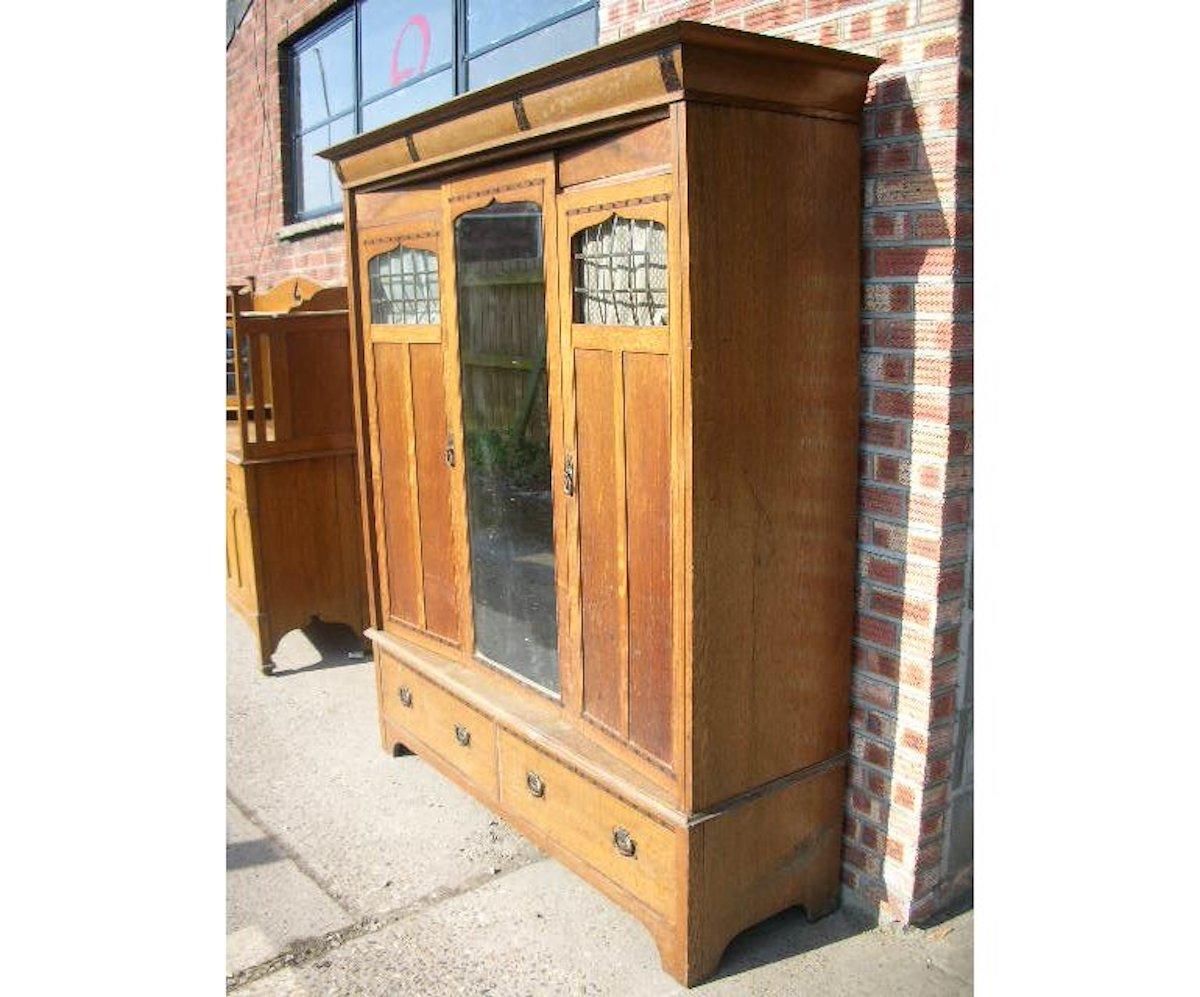 Gillows. An Arts & Crafts Glasgow style Arts & Crafts oak treble wardrobe with ebony and walnut stylized floral inlays to the cornice and further leaf style inlays to the door tops and bottoms united by vertical ebony line inlay. With a central door