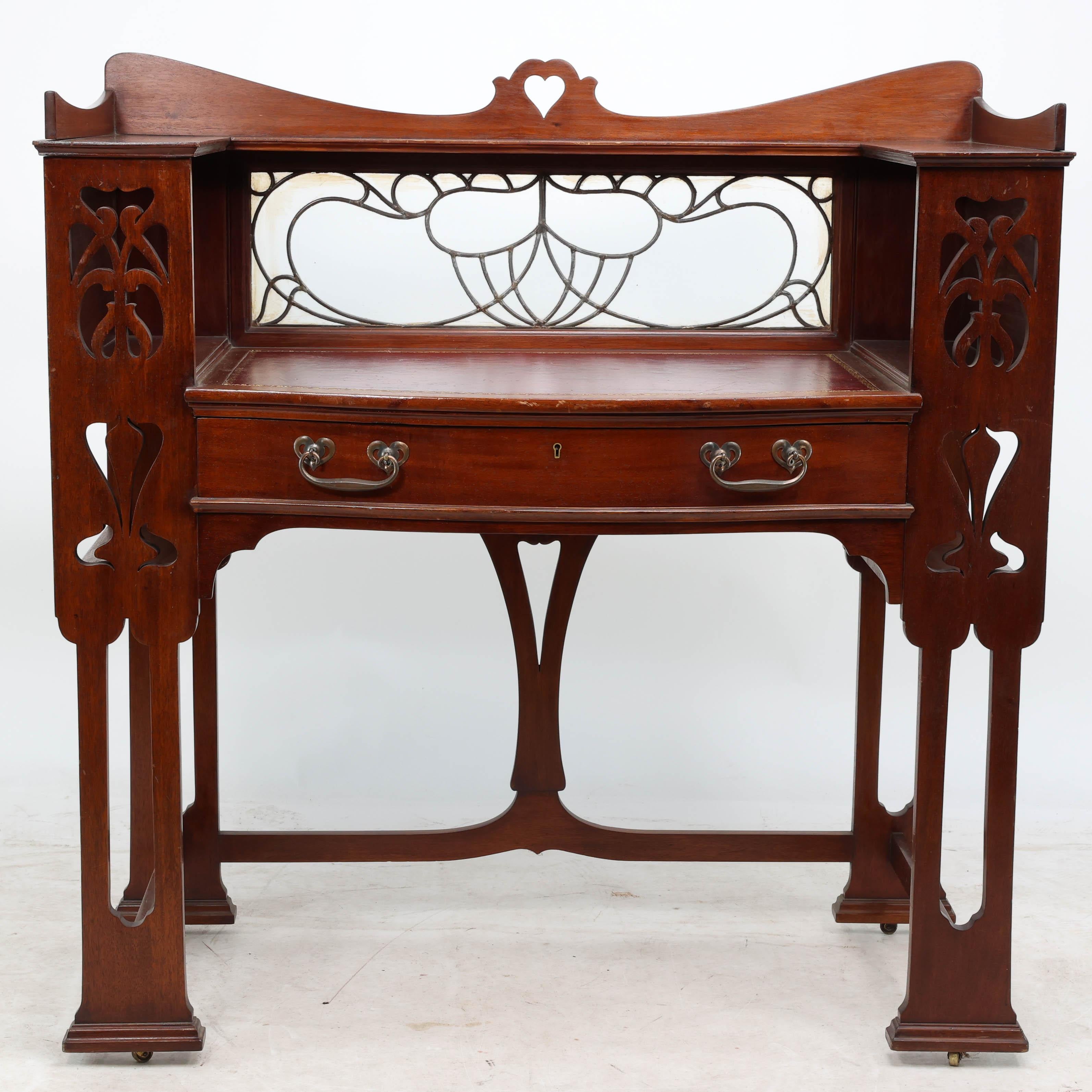 Shapland & Petter. Splendido scrittoio in mogano Arts & Crafts con cuore traforato nella parte superiore, schienale e lati sagomati, ripiano superiore a tre quarti e schienale in vetro piombato floreale stilizzato nella parte inferiore. Area di