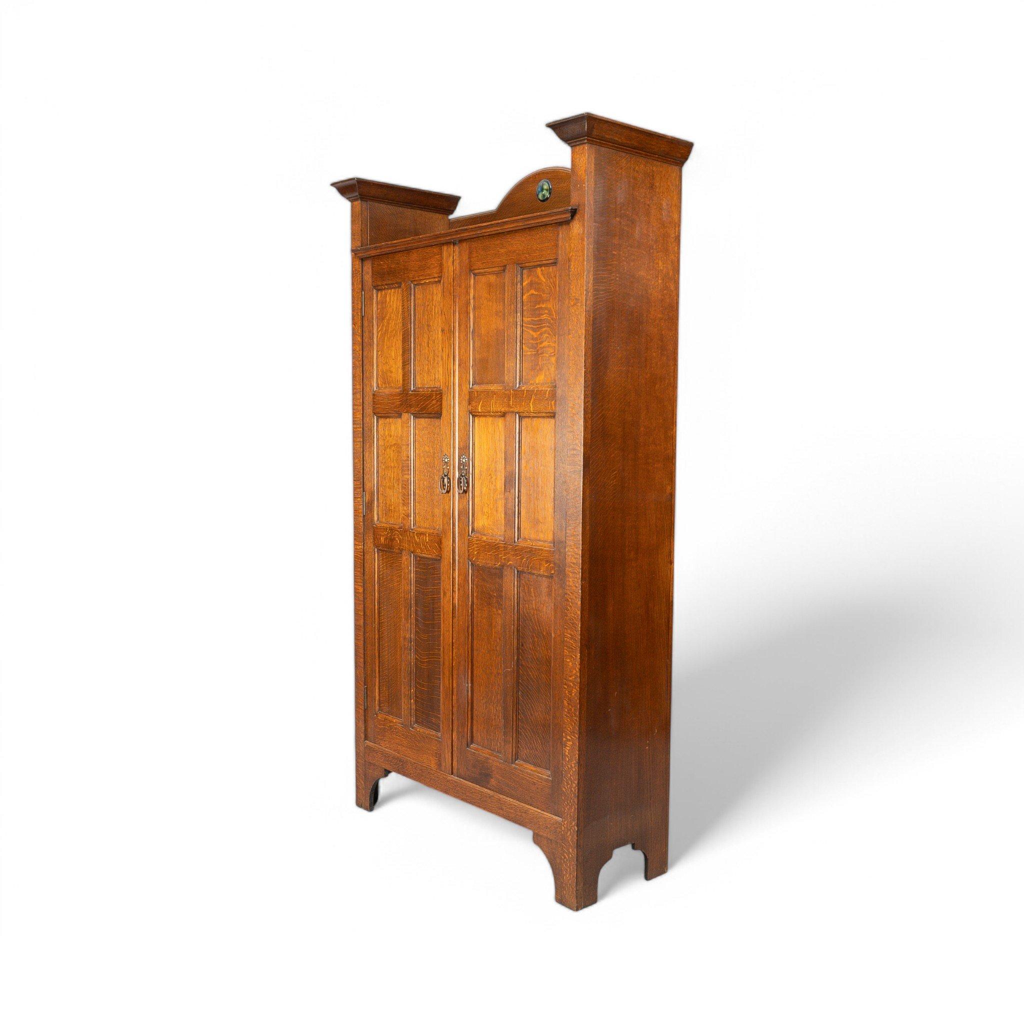 Shapland & Petter
Se trata de un armario de recibidor Arts and Crafts de roble con una joya circular Ruskin en la parte superior y un estante para guardar sombreros en la parte superior.
Las puertas dobles se abren para dejar espacio para colgar y